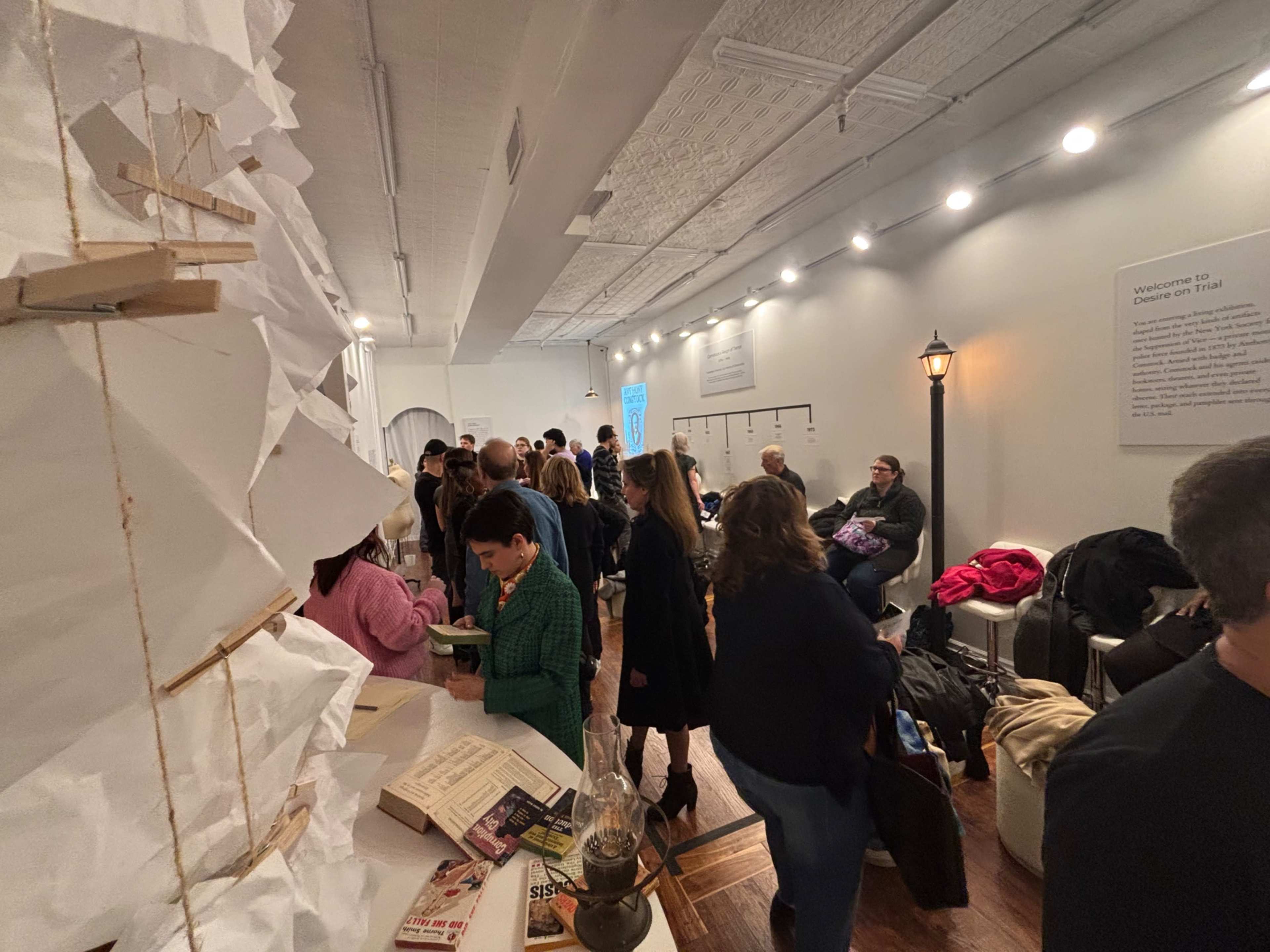 A crowded event space is filled with people engaging in conversation and activities around art installations and informational displays.