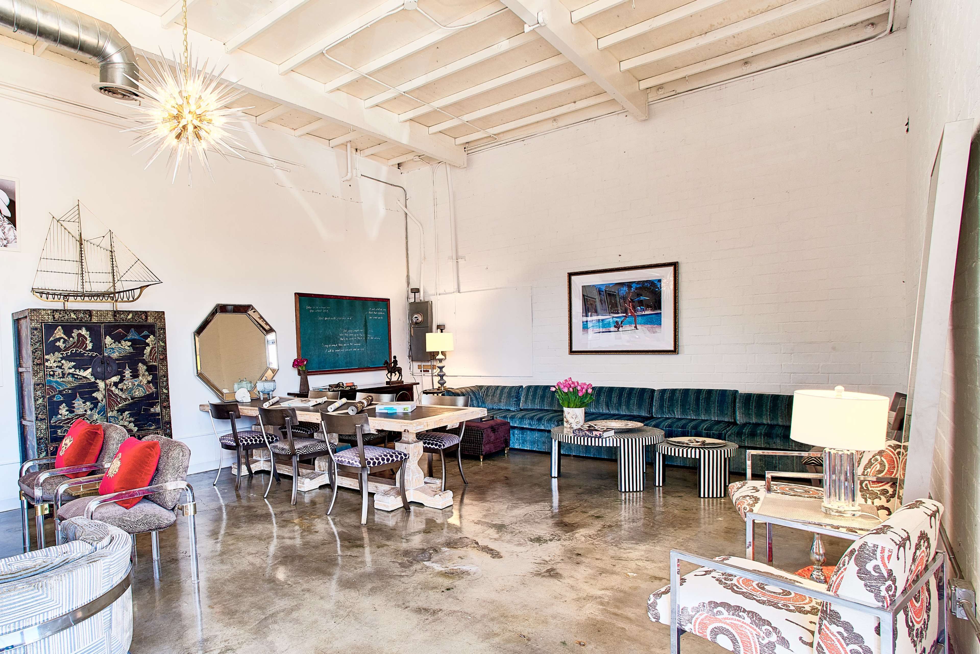 The image shows a spacious room with a green velvet couch, various chairs, and a central table, all set against a backdrop of white walls and polished concrete flooring.