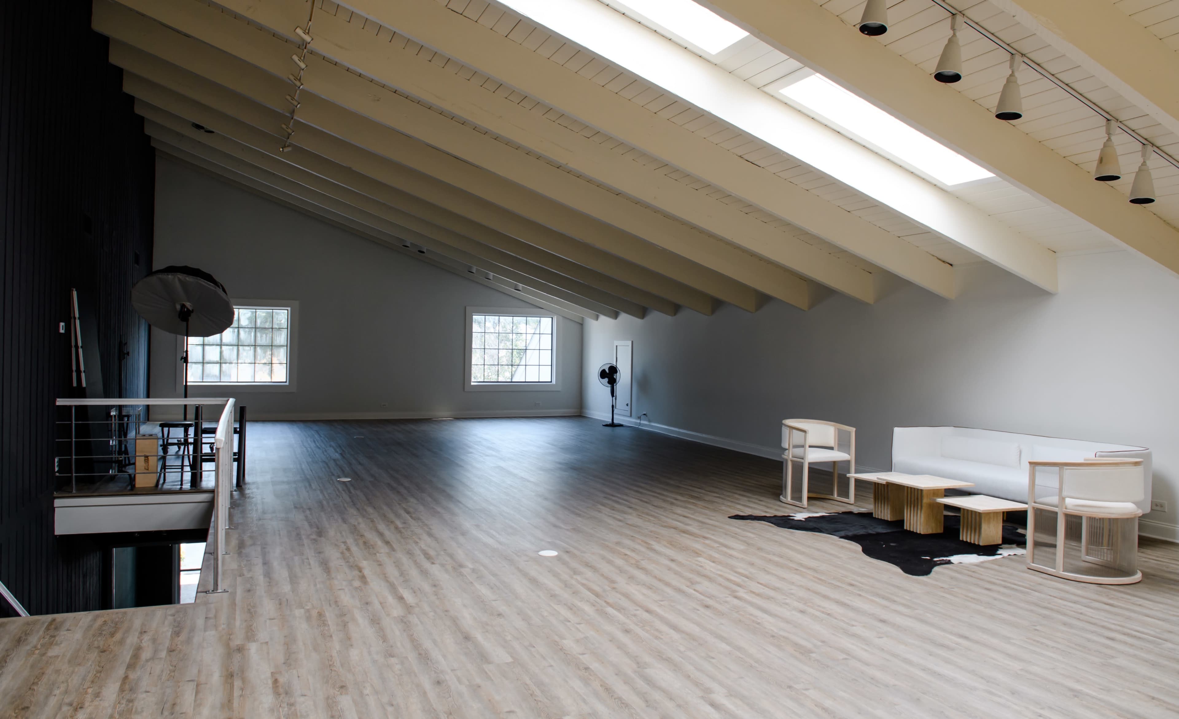 A spacious, well-lit room with high sloped ceilings, featuring wooden flooring, a white sofa, and minimalist furniture.