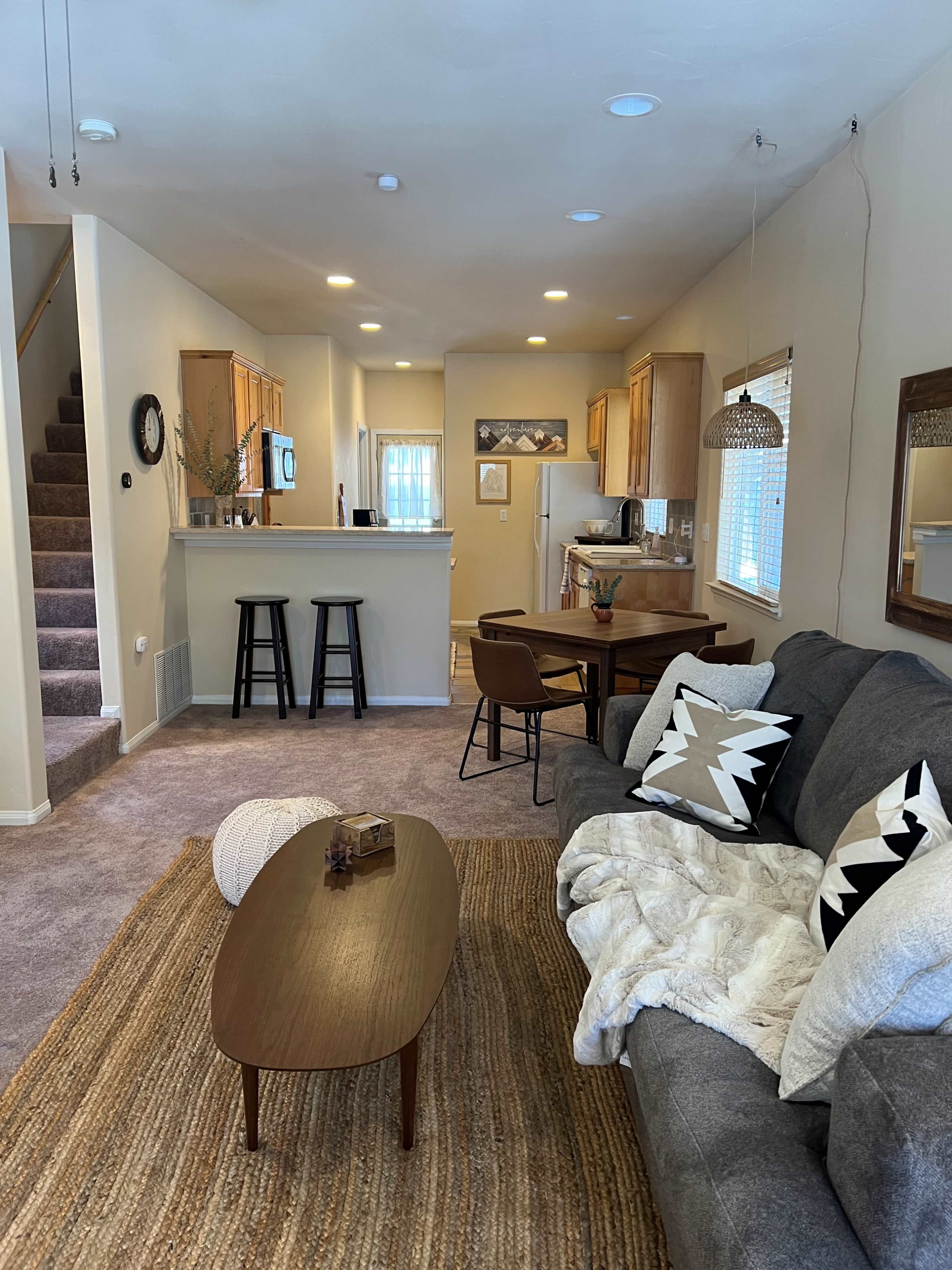A cozy living room area with a gray sofa, a coffee table, and a kitchen and dining space visible in the background.