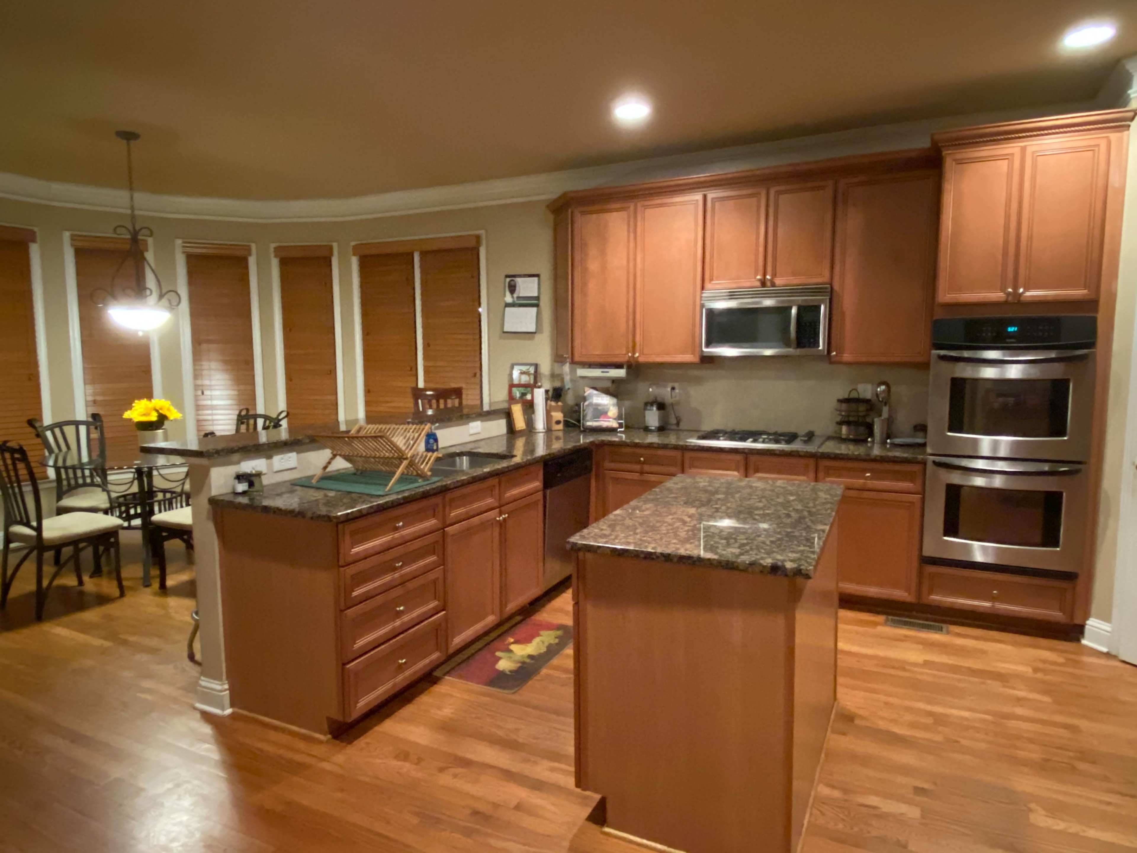 A kitchen with wooden cabinetry, granite countertops, and stainless steel appliances, featuring a dining area with a table and chairs nearby.