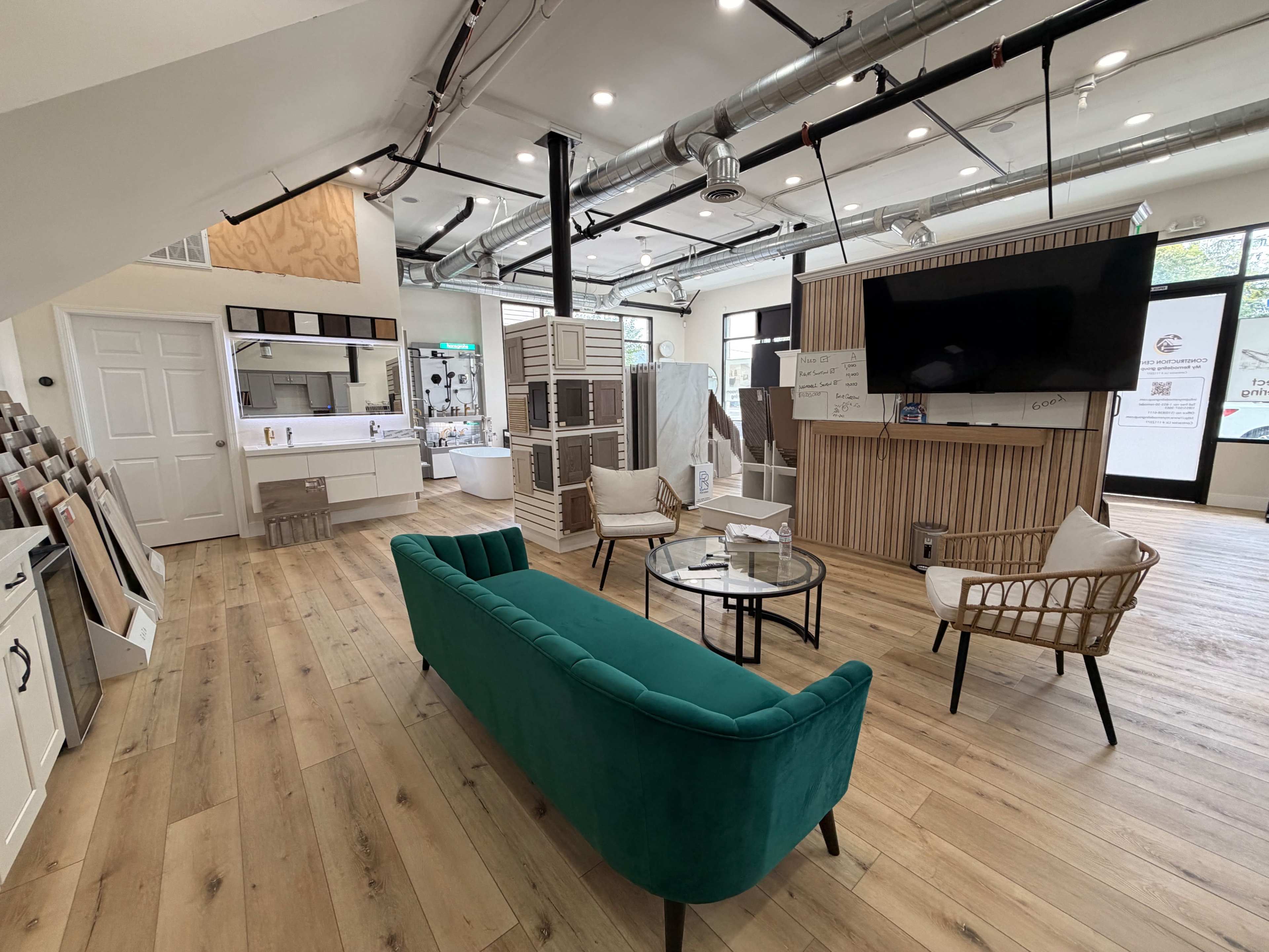 The image shows a modern showroom with a green sofa, a glass coffee table, and various display units featuring kitchen and bathroom designs.