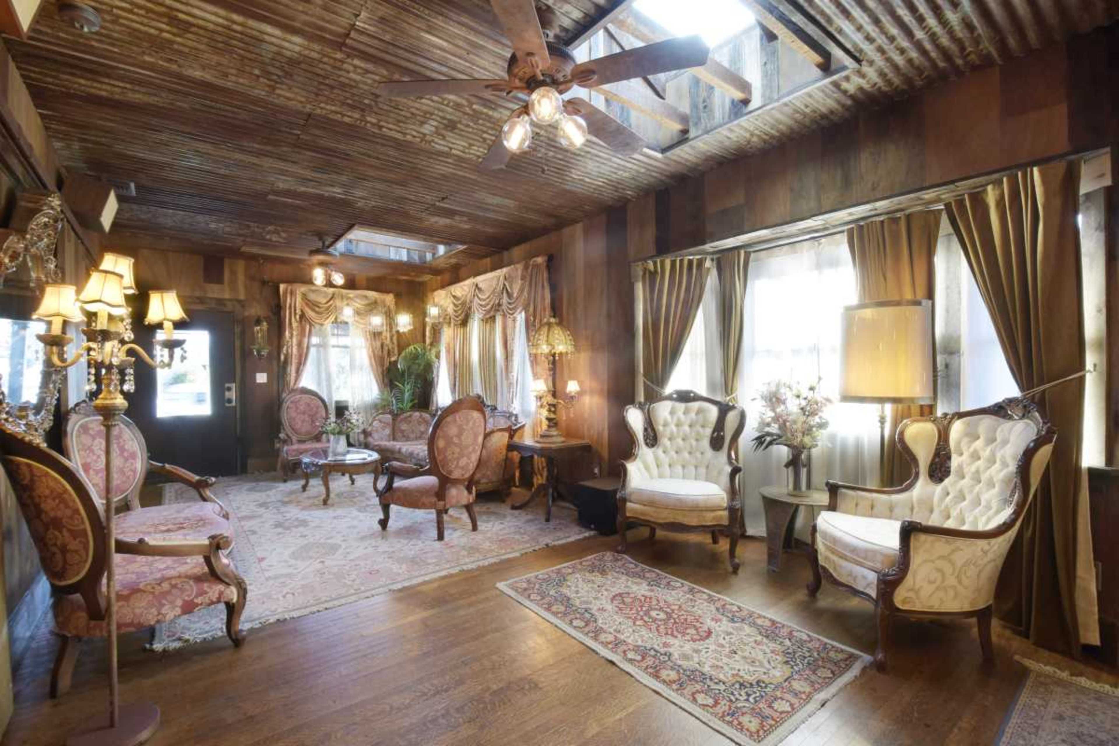 A cozy sitting room features vintage furniture, patterned rugs, and wooden walls with a rustic ceiling.