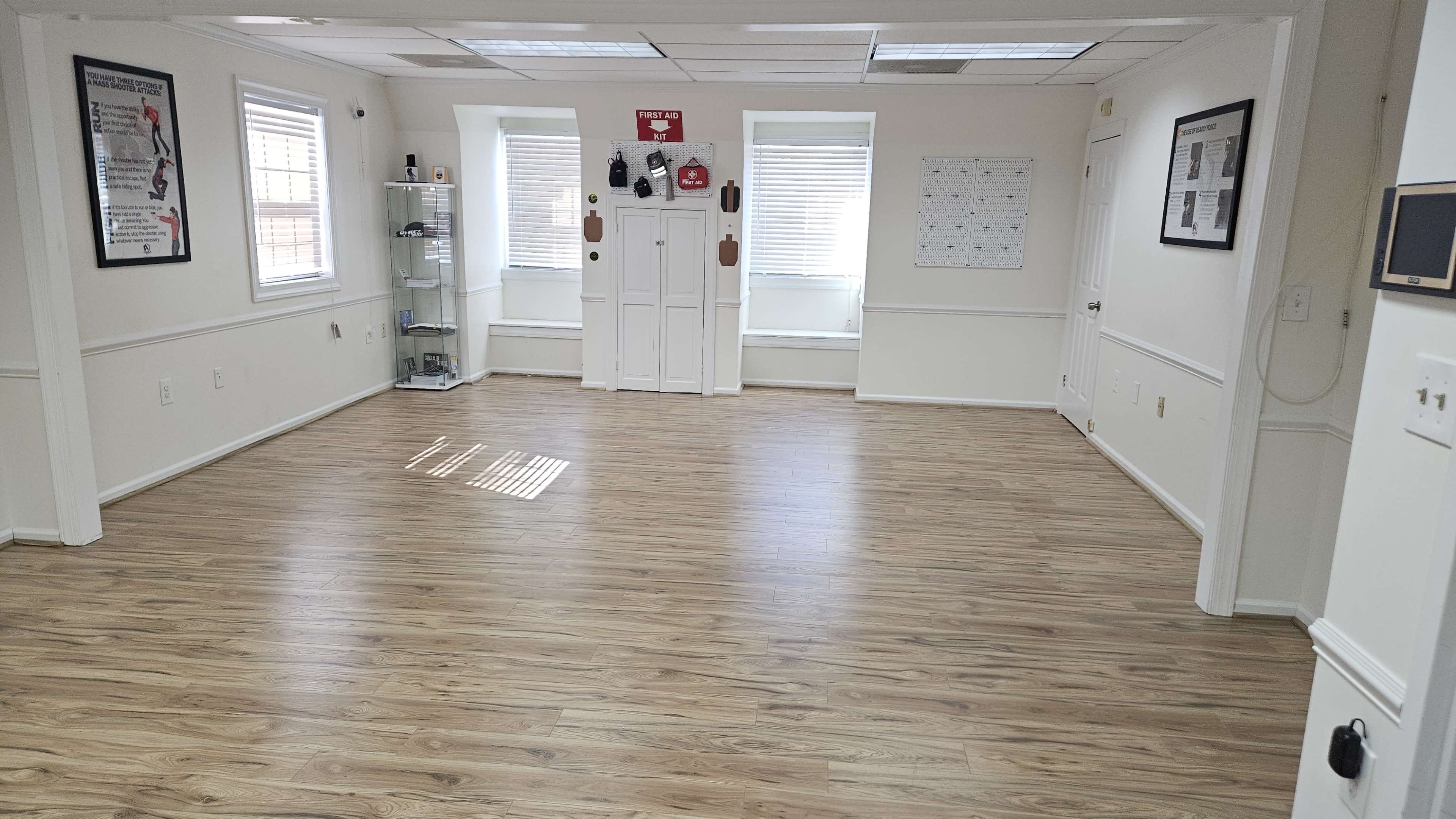 The image shows a large, empty room with wooden flooring, two windows, and a closet at the far end.