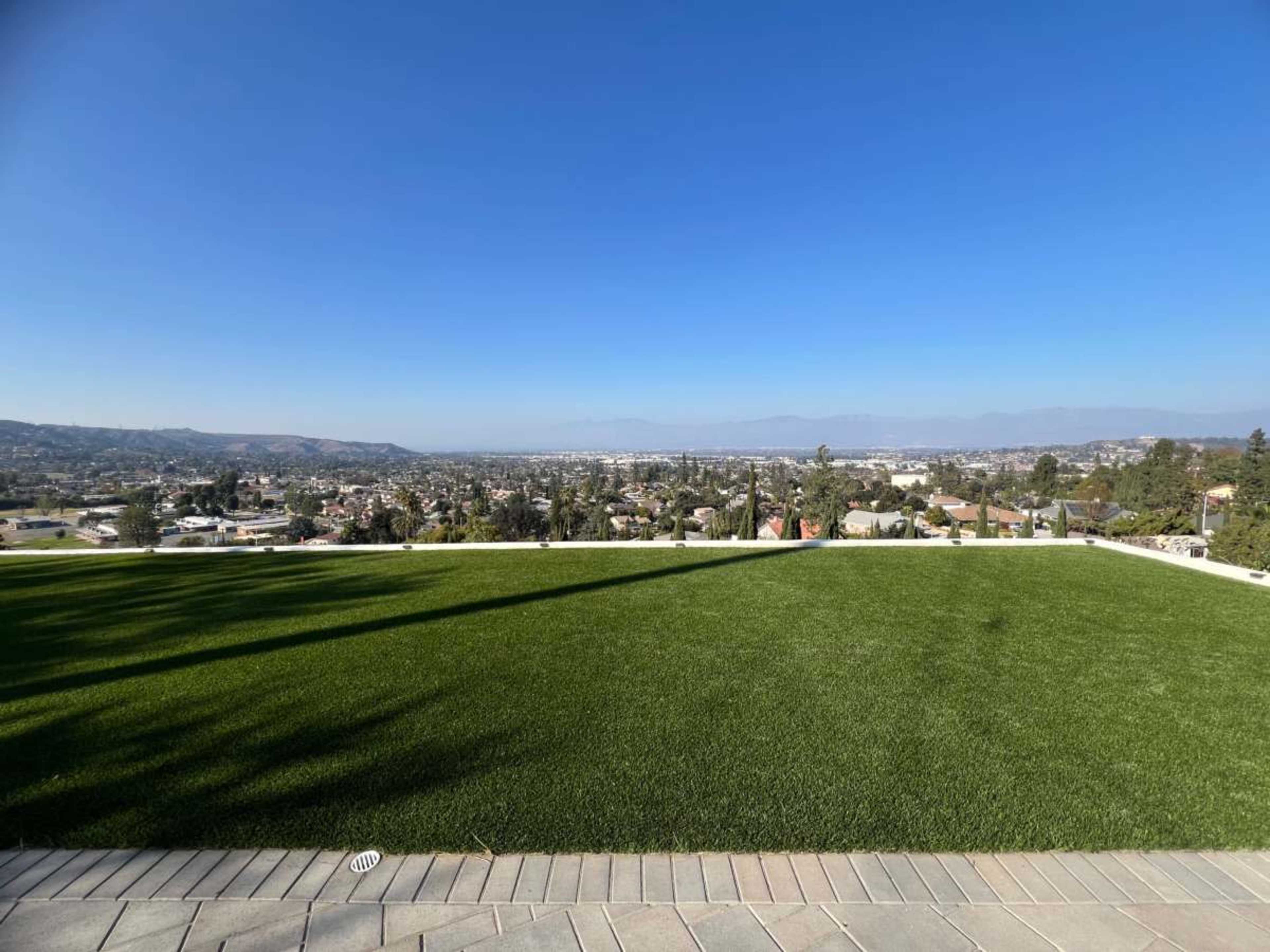 A flat, green lawn overlooks a sprawling cityscape and distant mountains under a clear blue sky.
