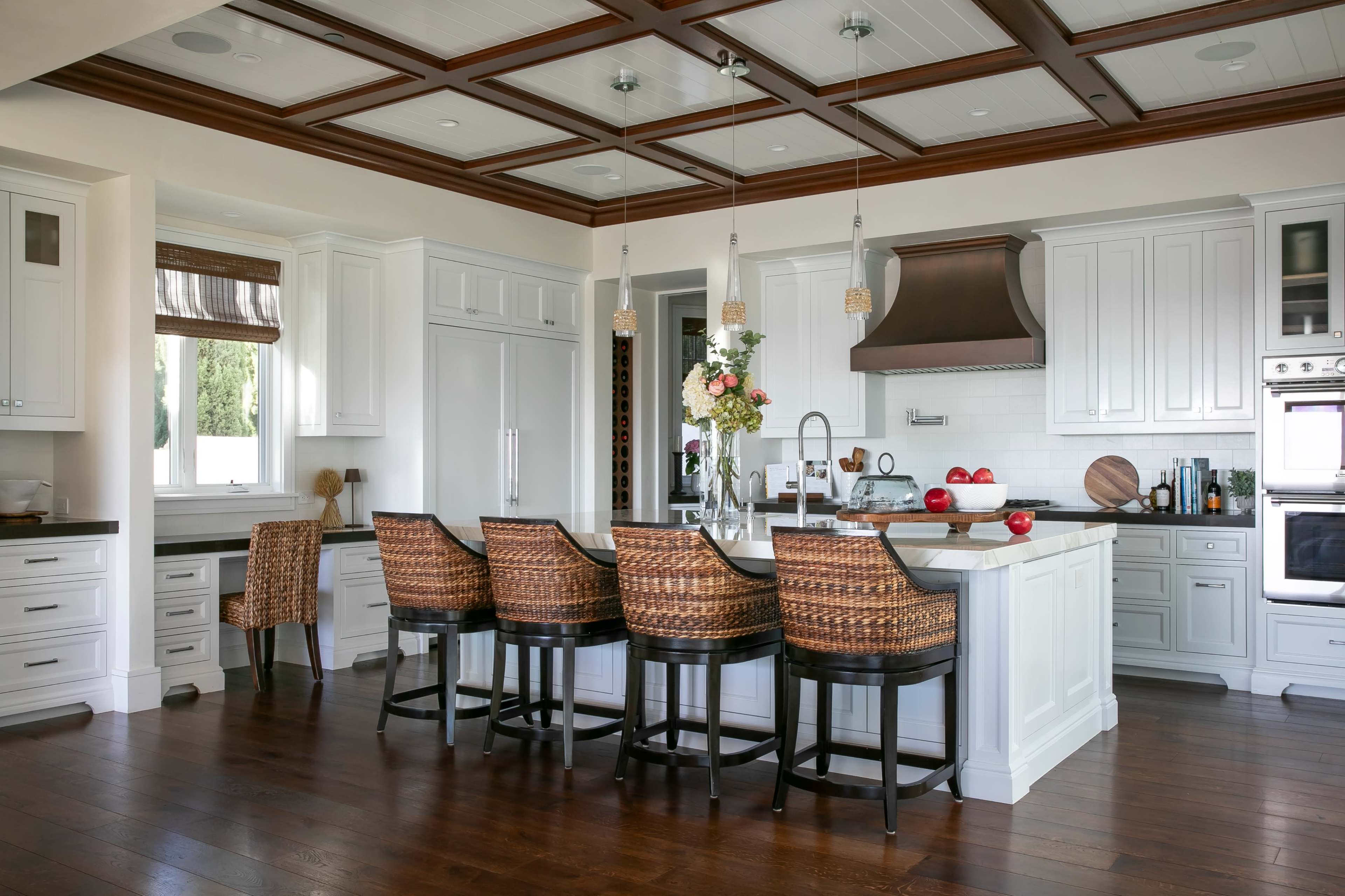 A modern kitchen features a large island with bar seating, white cabinetry, and wooden flooring.