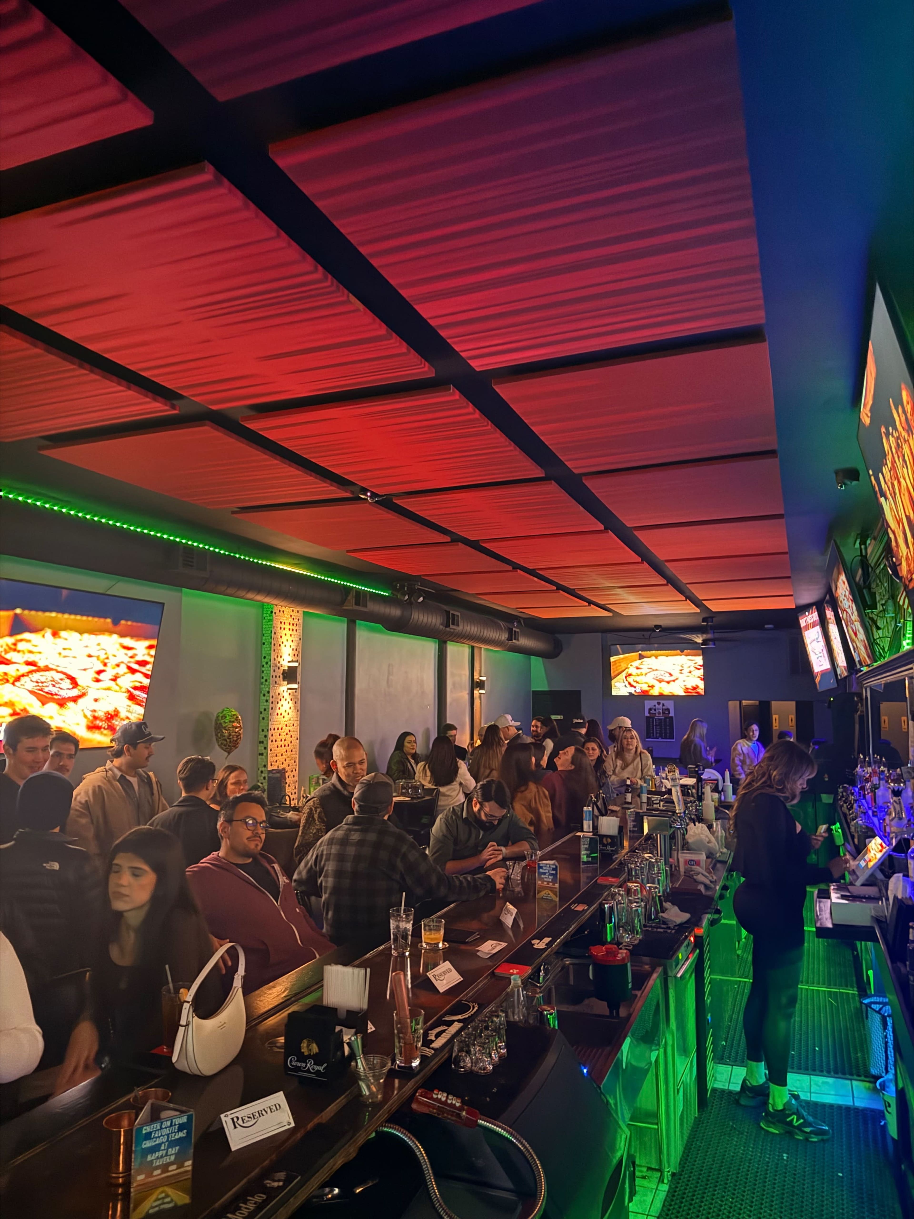 A crowded bar scene features patrons gathered at the counter, with glowing neon lights and large screens displaying images.