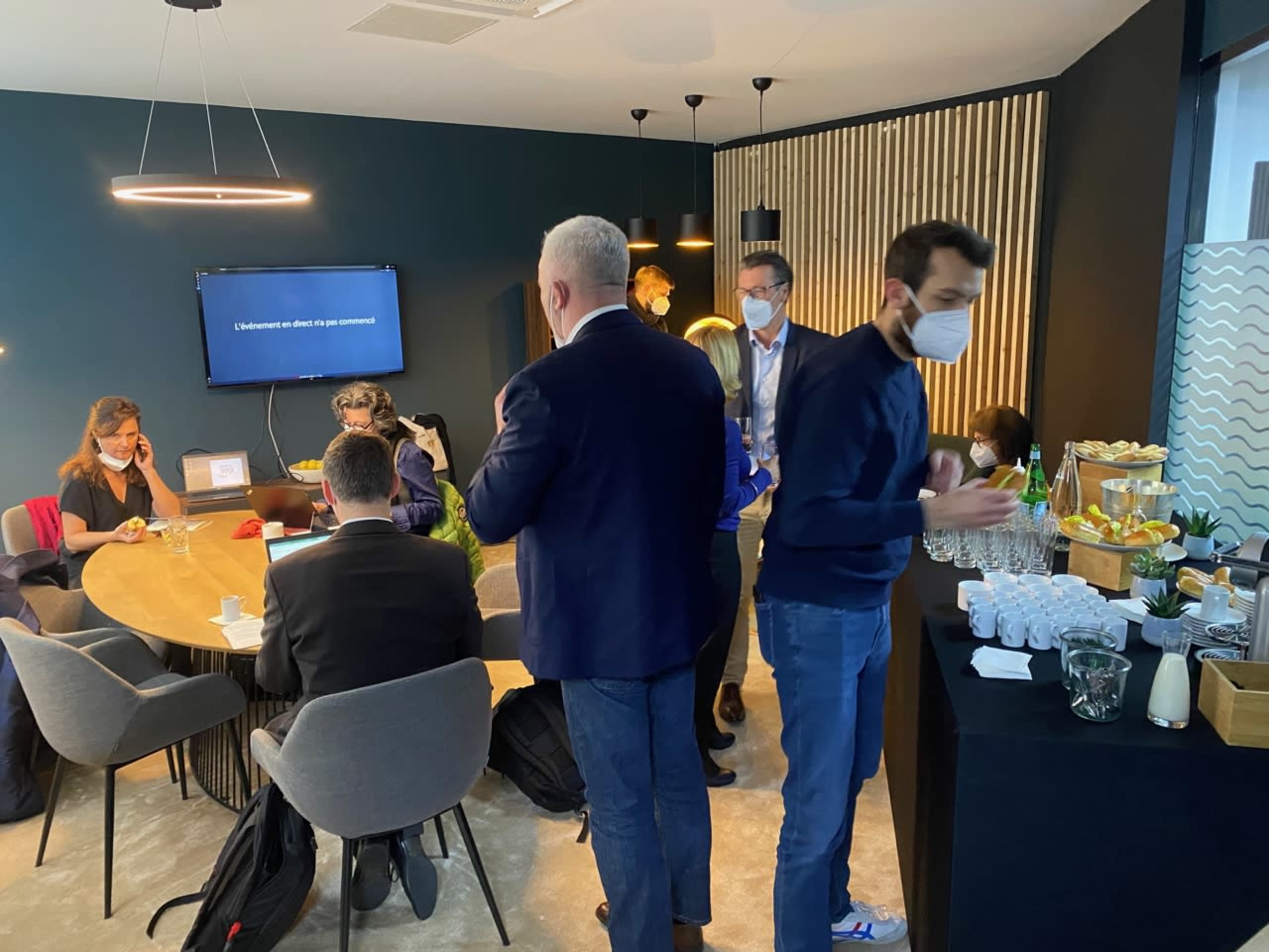 A group of people are engaged in conversation and activities in a modern meeting room, with a buffet table set up in the corner.