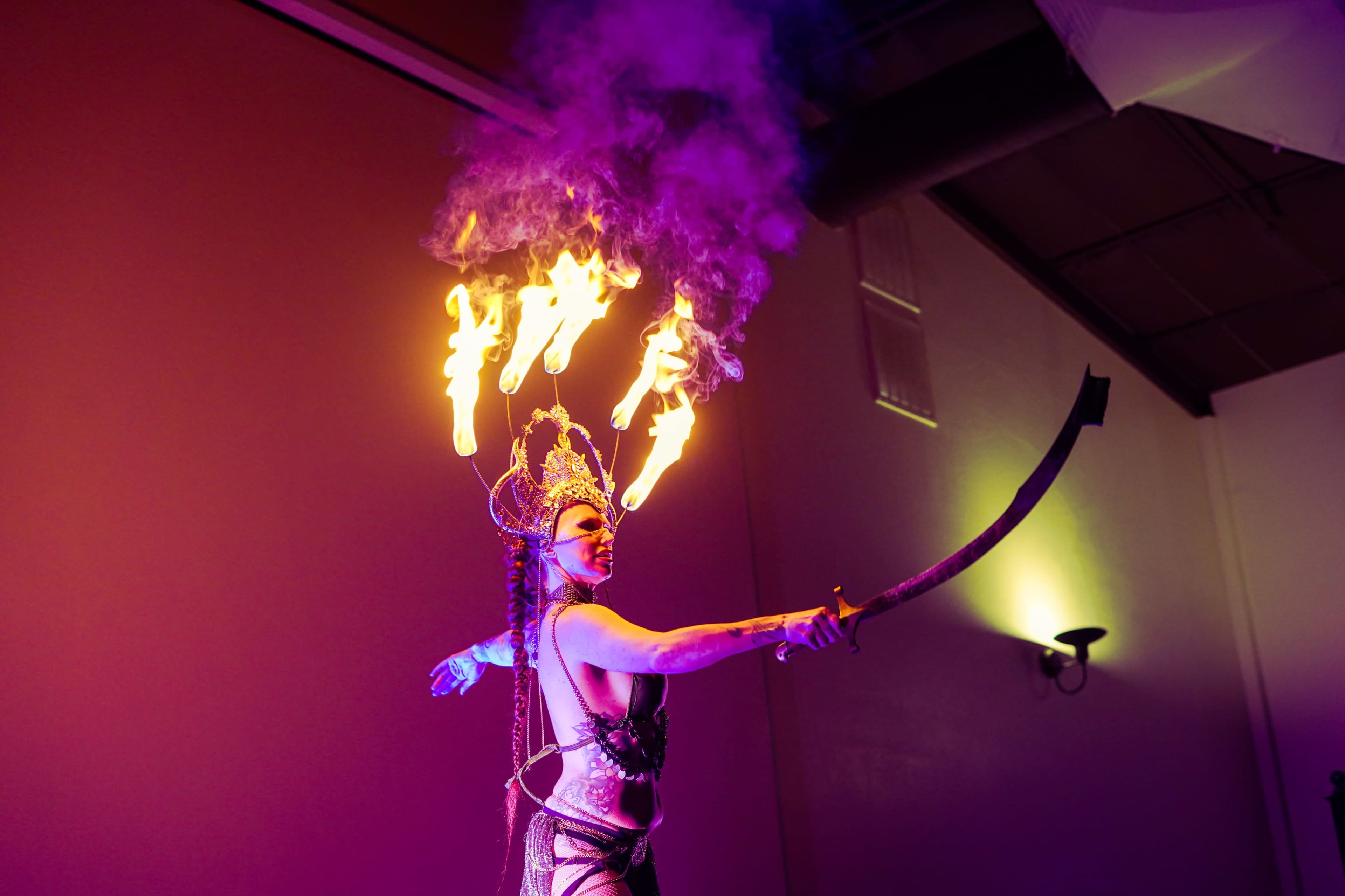 A performer showcases fire dancing, wielding flaming torches while wearing elaborate costume and makeup.