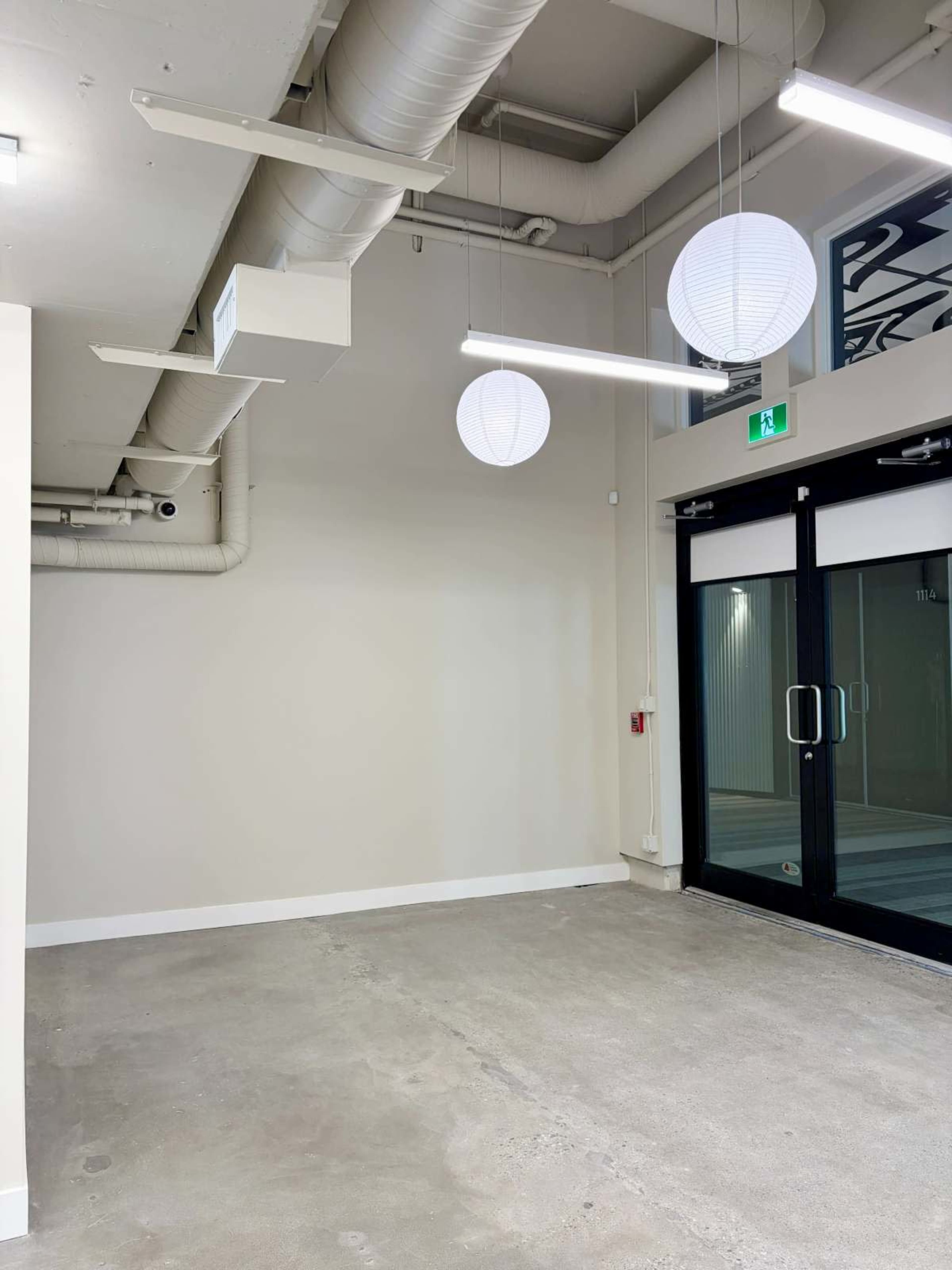 The image shows an empty interior space with concrete flooring, white walls, and three round pendant lights hanging from the ceiling.