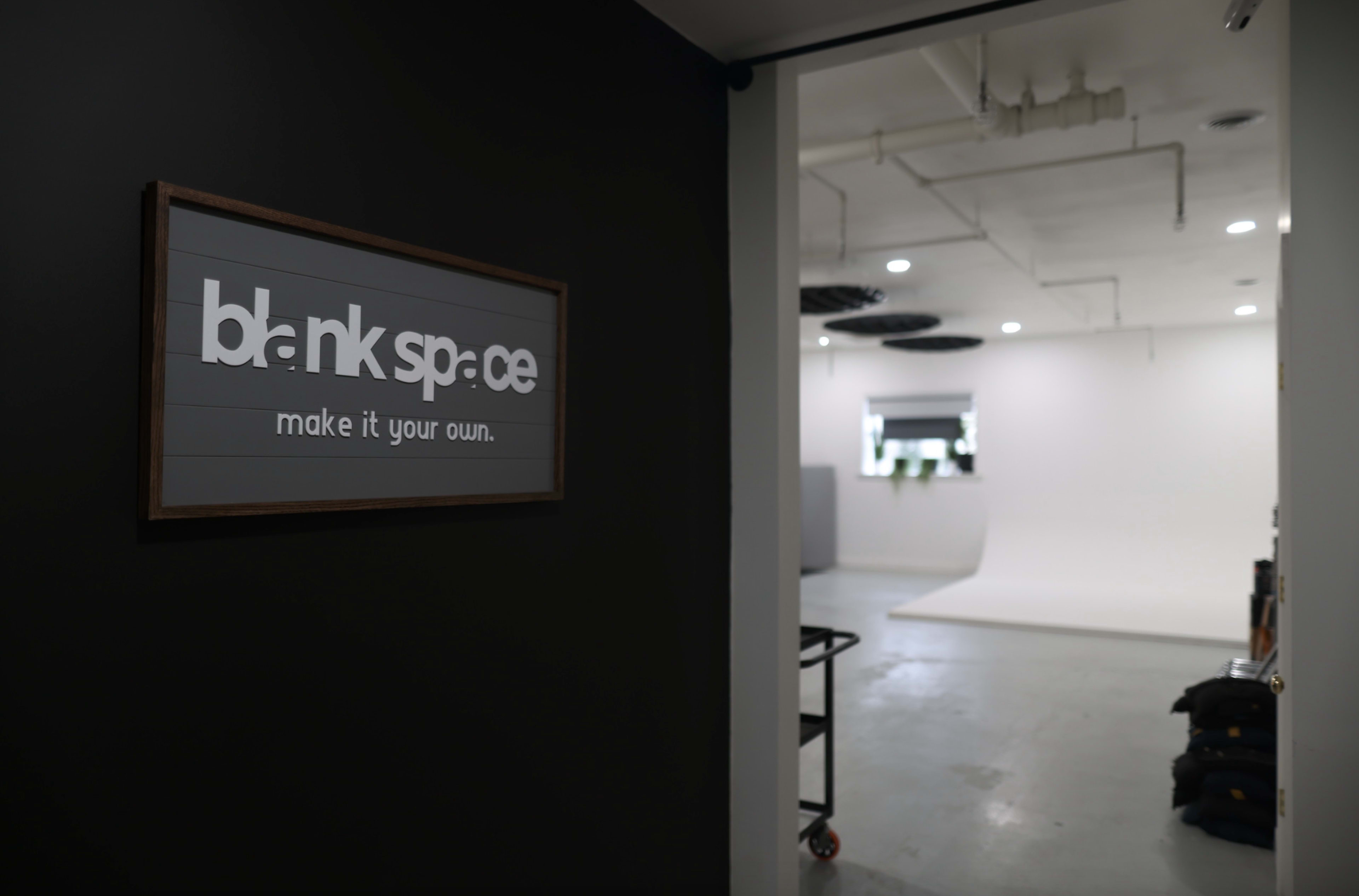 A sign reading "blank space" is mounted on a wall, leading to a brightly lit studio area with a white backdrop.