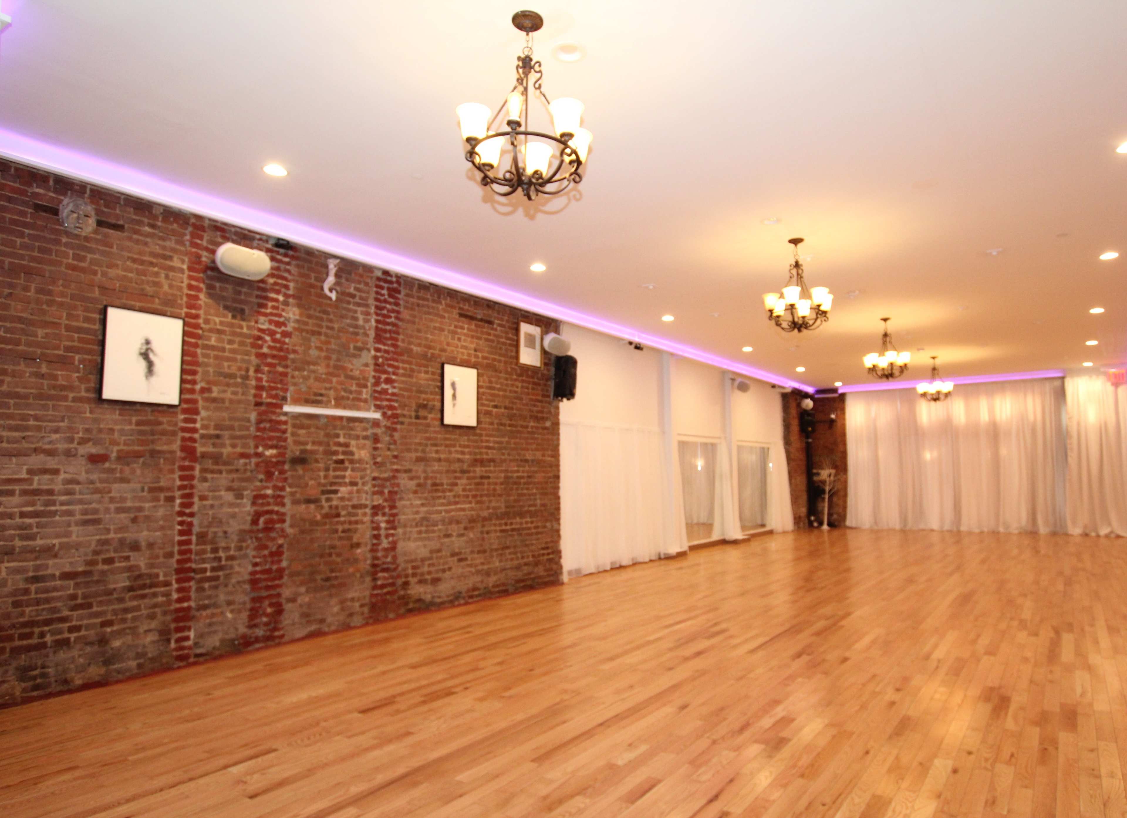 A spacious indoor venue with exposed brick walls, hardwood flooring, and chandeliers, illuminated by soft lighting.