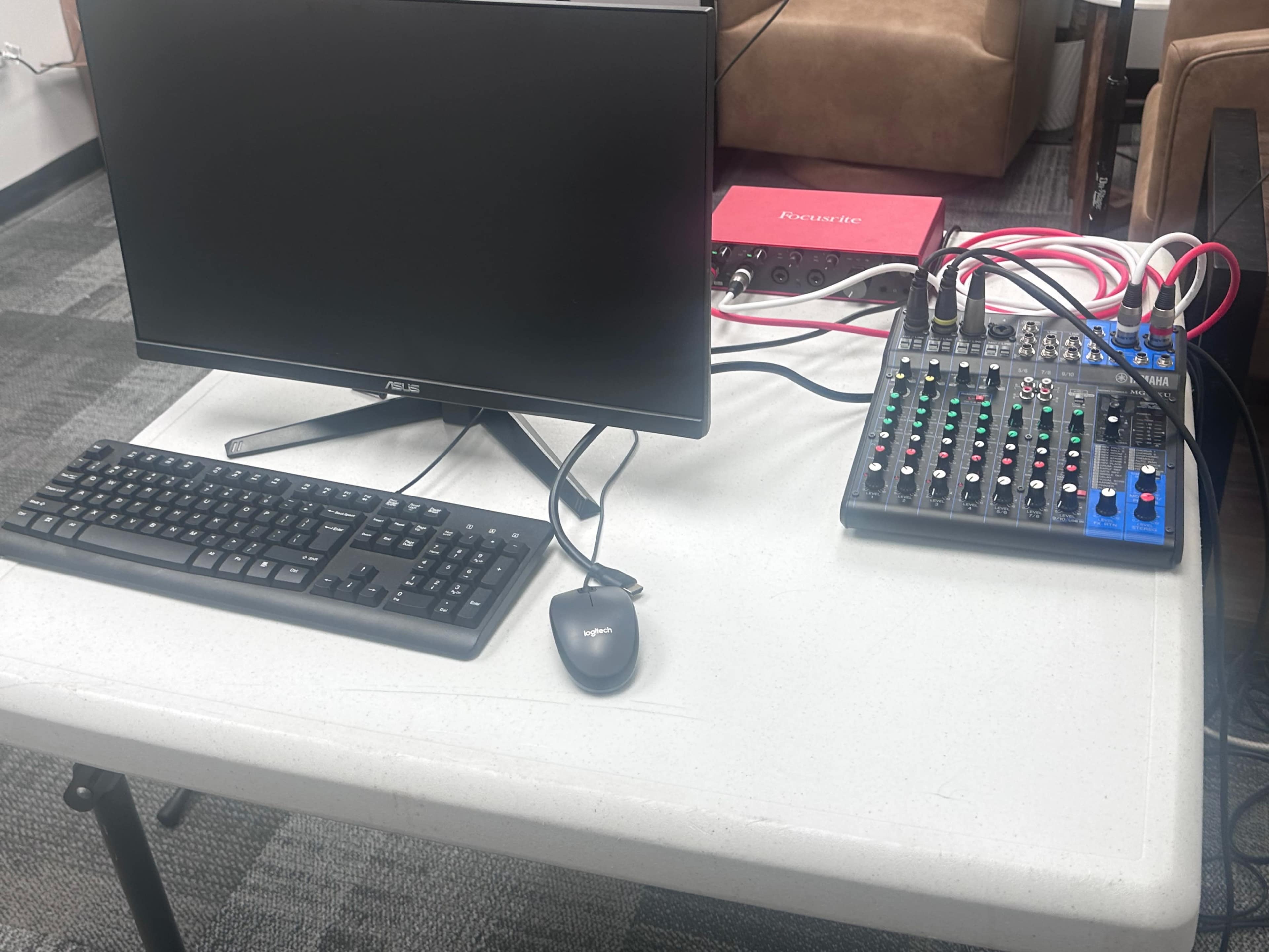The image shows a table with a computer monitor, keyboard, mouse, and an audio mixer with various colored cables connected to it.