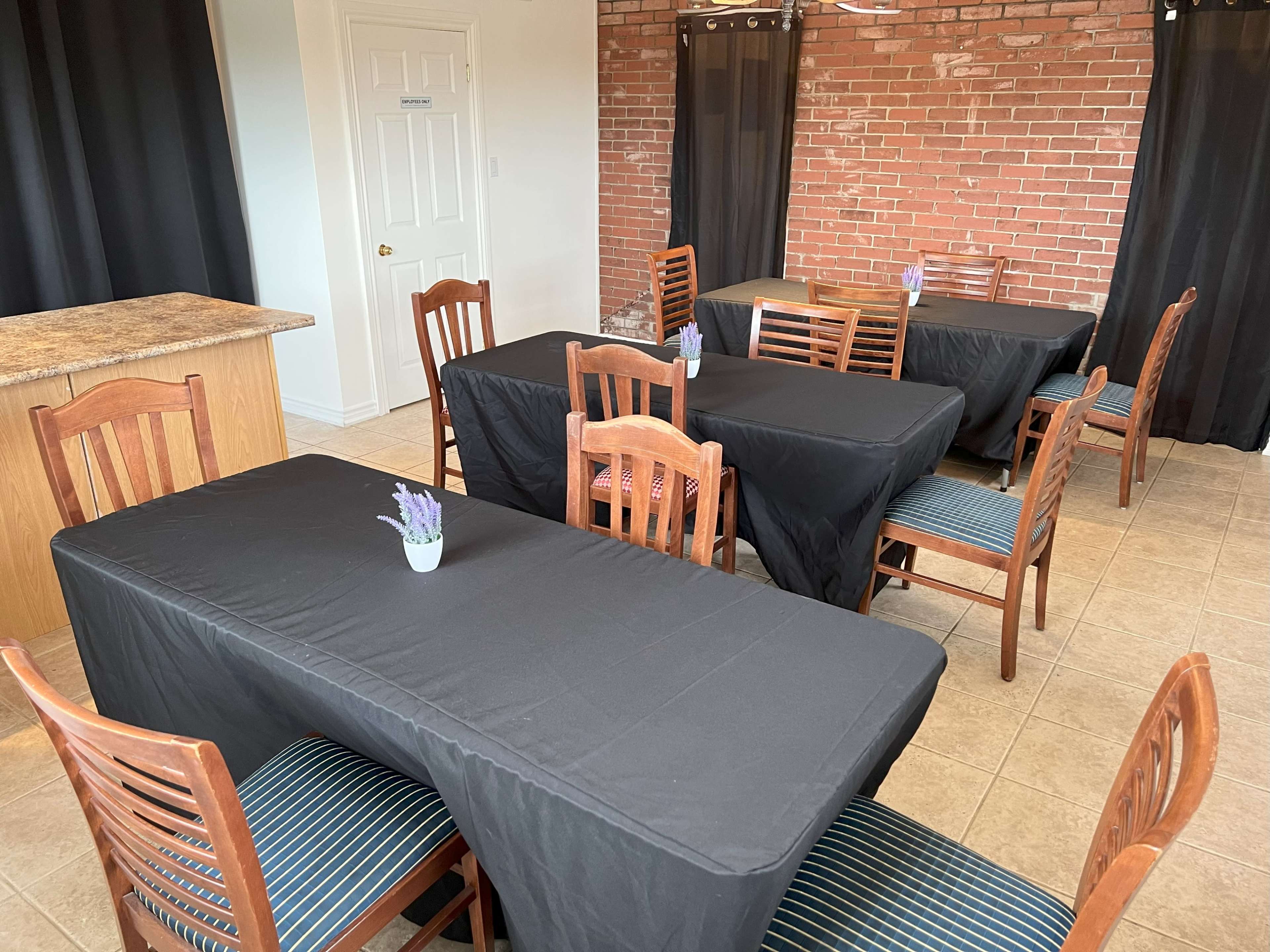 A room with several tables covered in black tablecloths and wooden chairs, arranged around a small vase with lavender on each table.