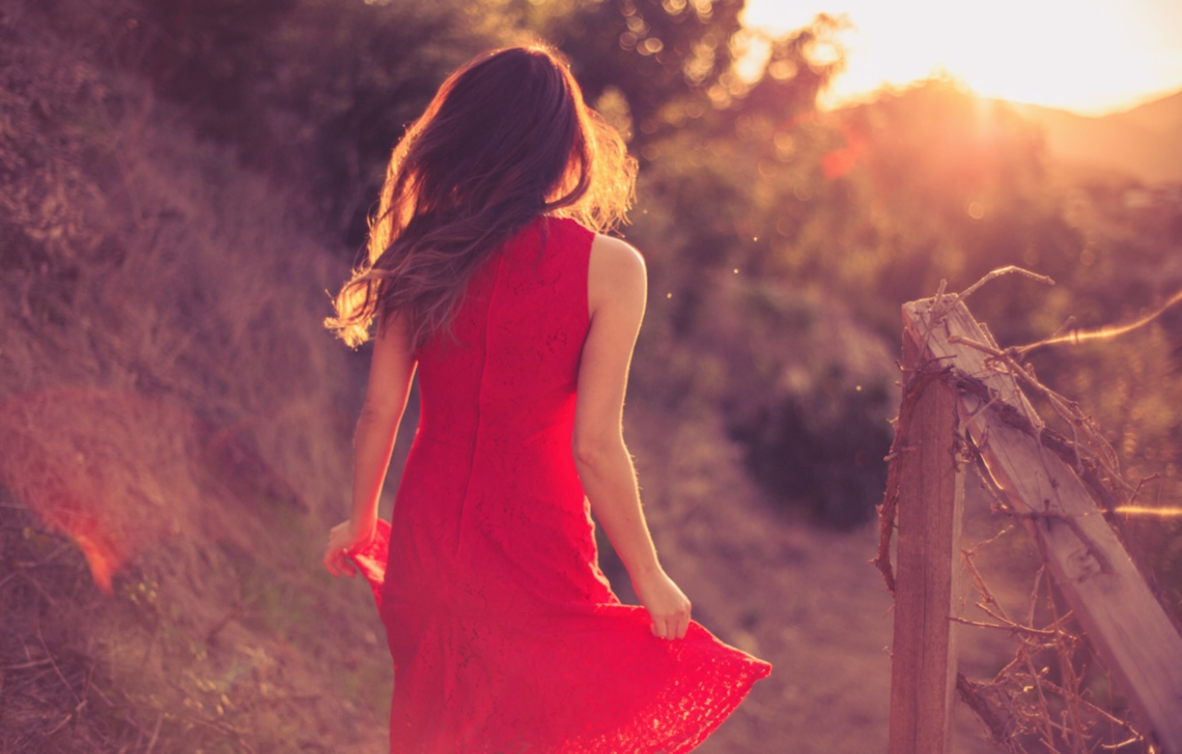 A woman in a red dress walks along a sunlit path surrounded by greenery.