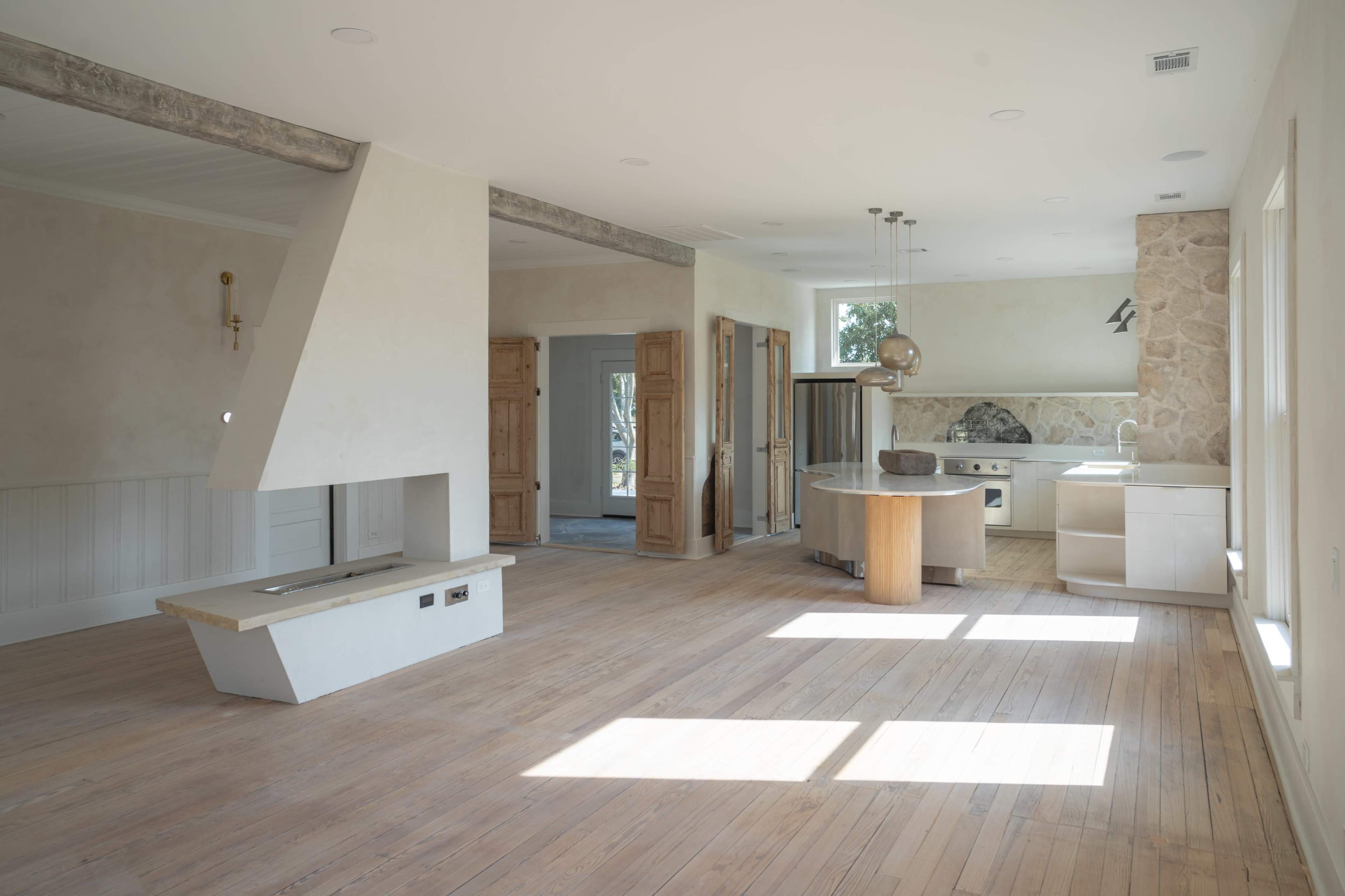 A spacious, unfinished interior of a modern house with wooden floors, large windows, and a kitchen area integrated into the main living space.