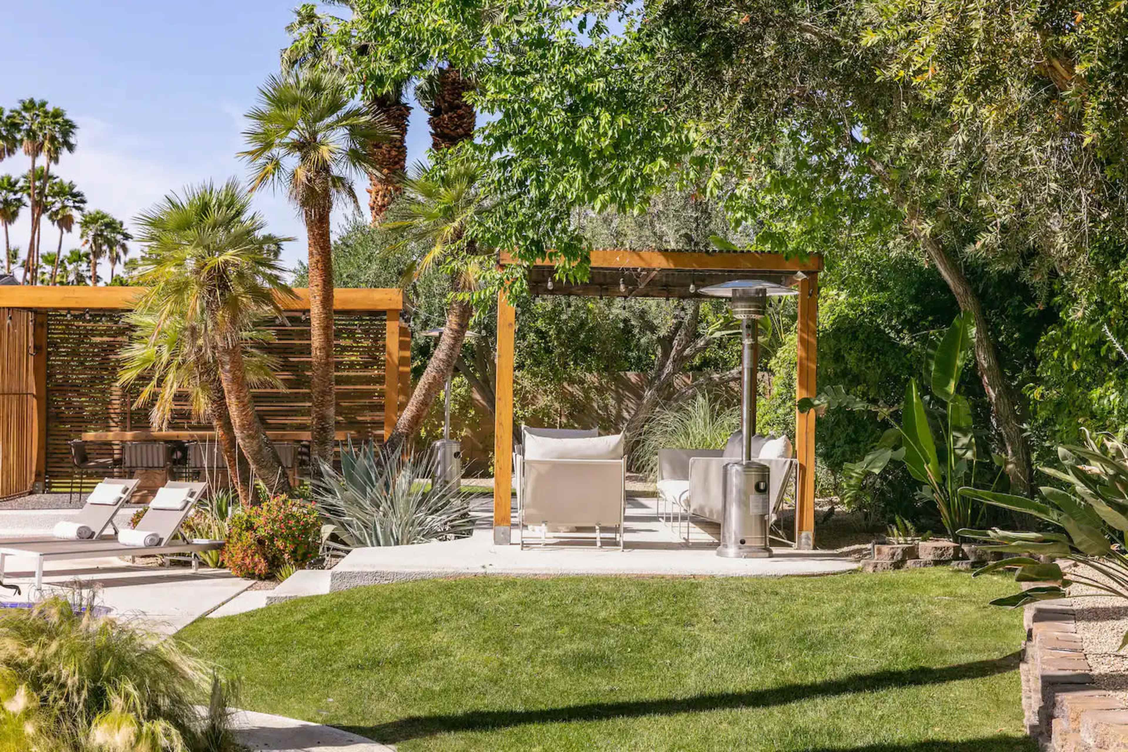 A landscaped outdoor space featuring a seating area with white chairs, surrounded by greenery and palm trees.