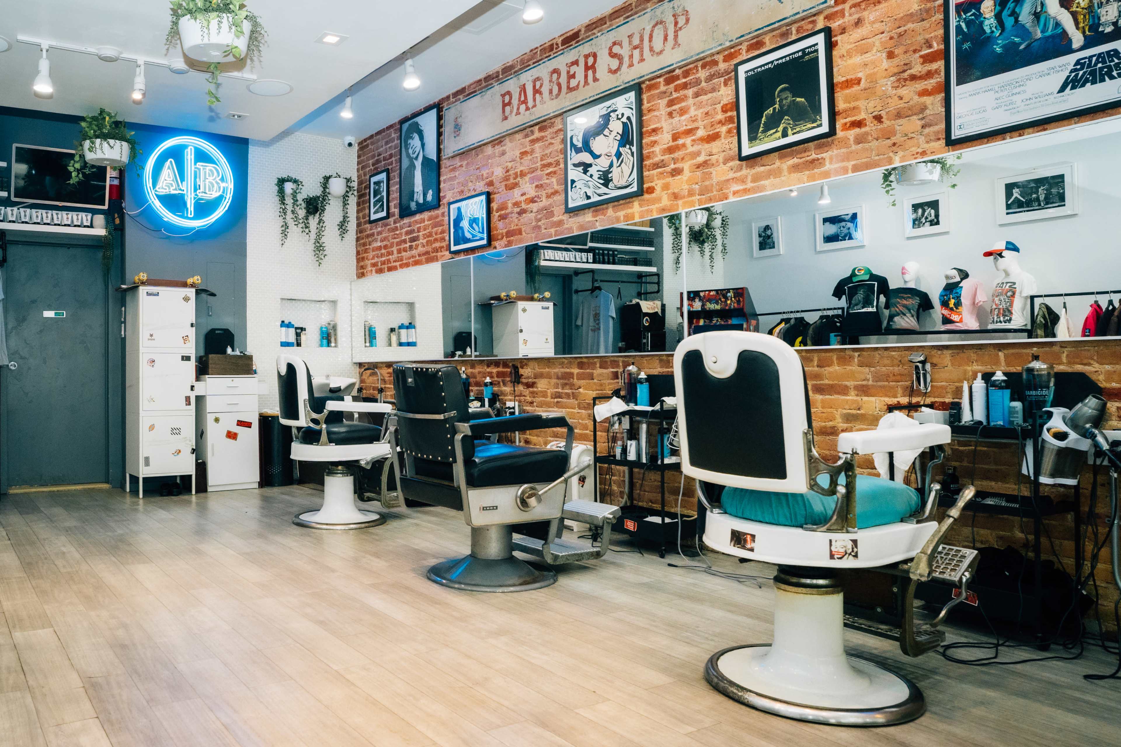 A modern barber shop interior featuring two vintage barber chairs, wall mirrors, and a brick wall adorned with posters and a blue neon sign.