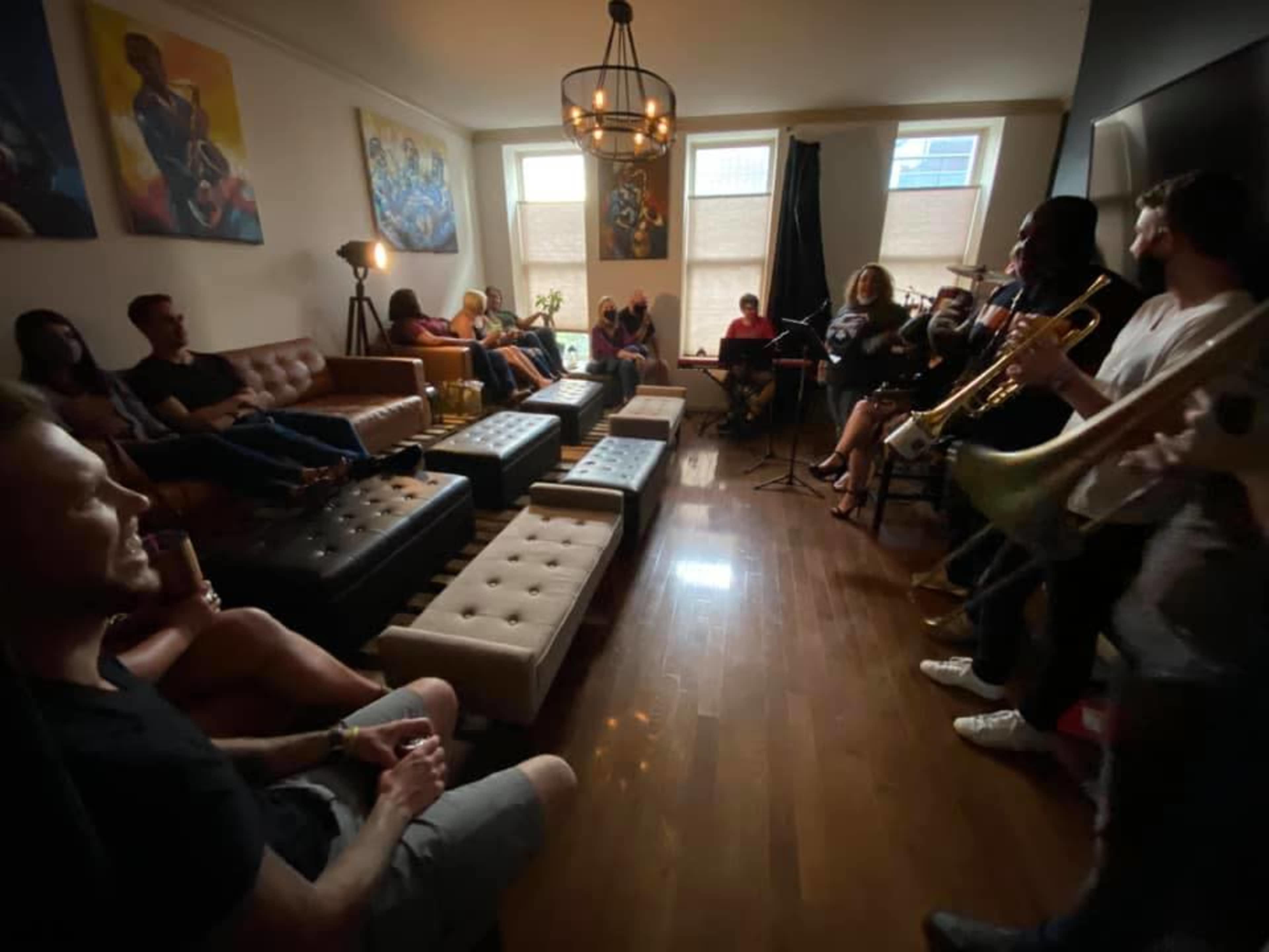 A group of people are seated in a cozy living room while a small band performs music in the corner.
