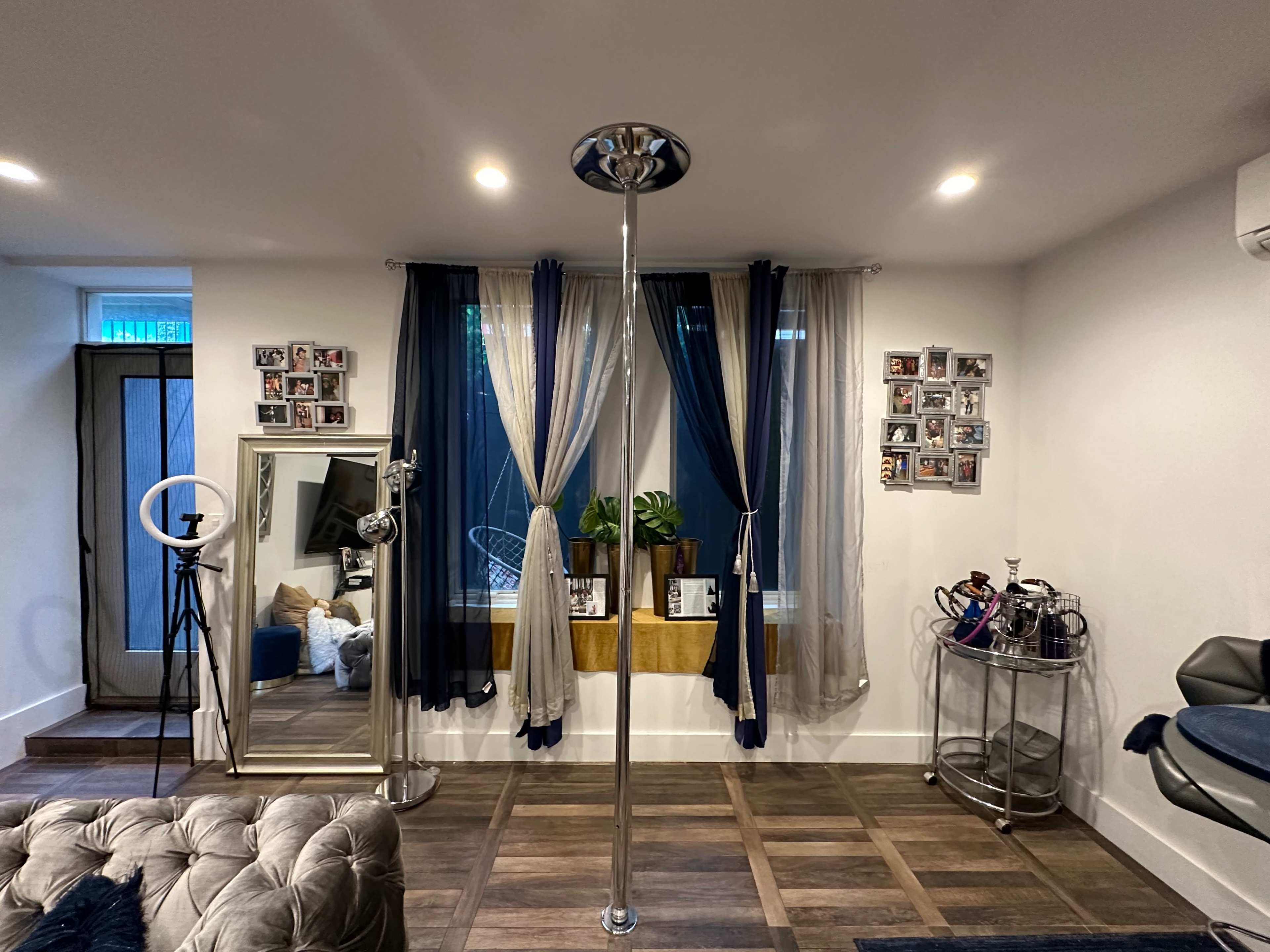 A well-decorated room featuring a mirrored pole, a large window with drapes, and framed photos on the wall.