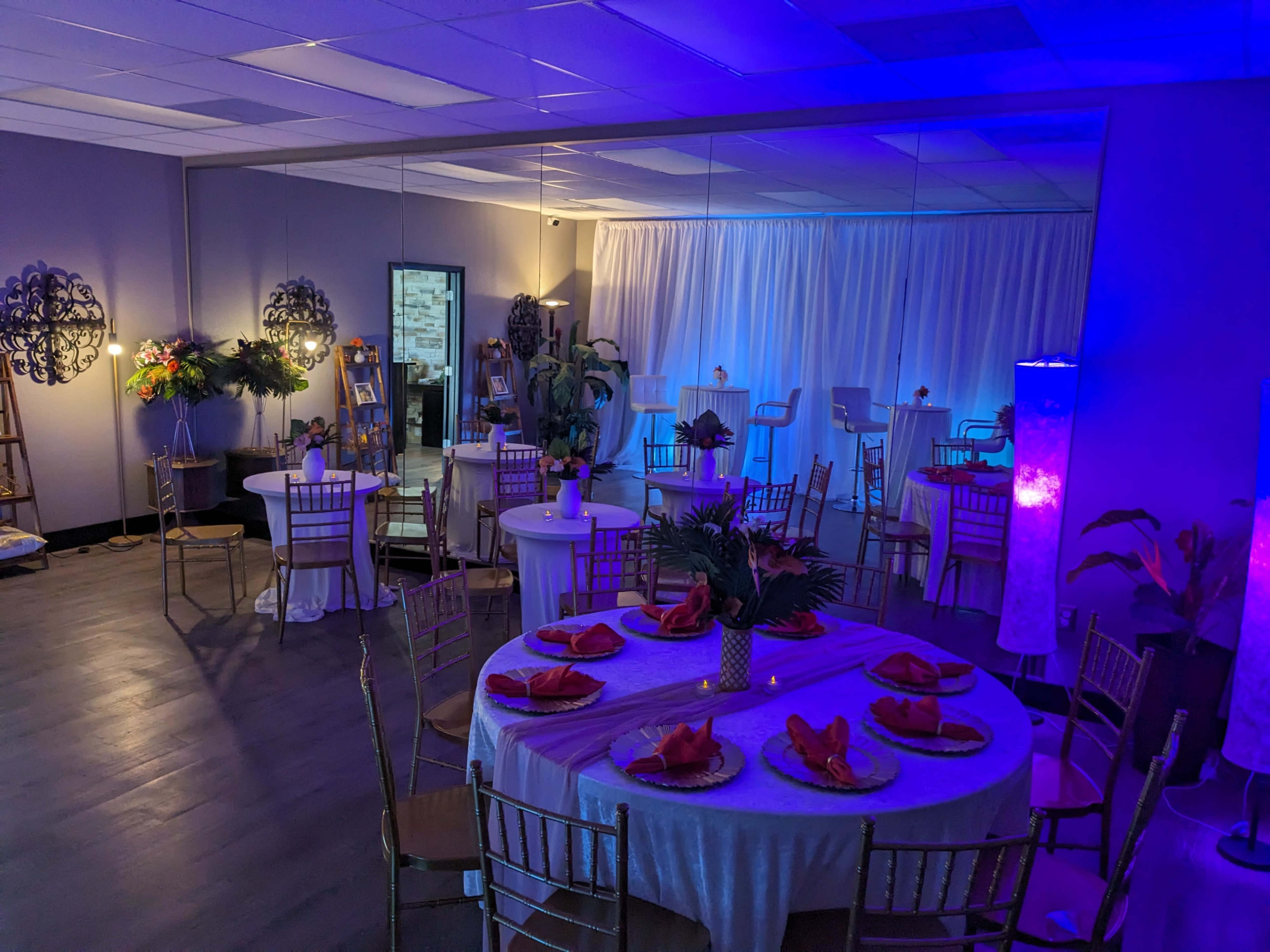 The image shows a decorated event space with tables set for dining, illuminated by soft lighting, and featuring a mirrored wall.