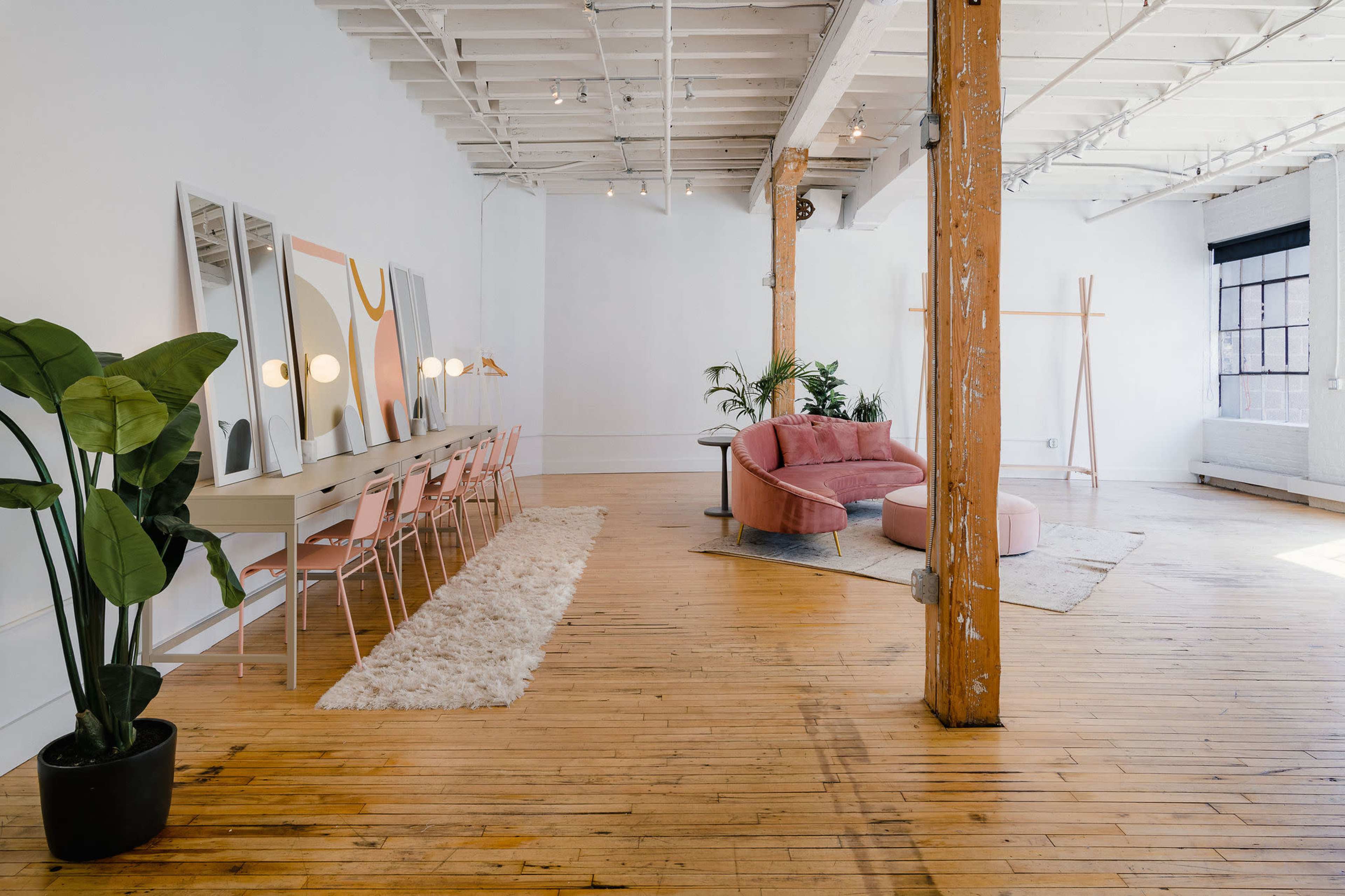 A spacious, modern interior with wooden floors, a pink sofa, a light-colored dining table with pink chairs, and large mirrors on the wall.