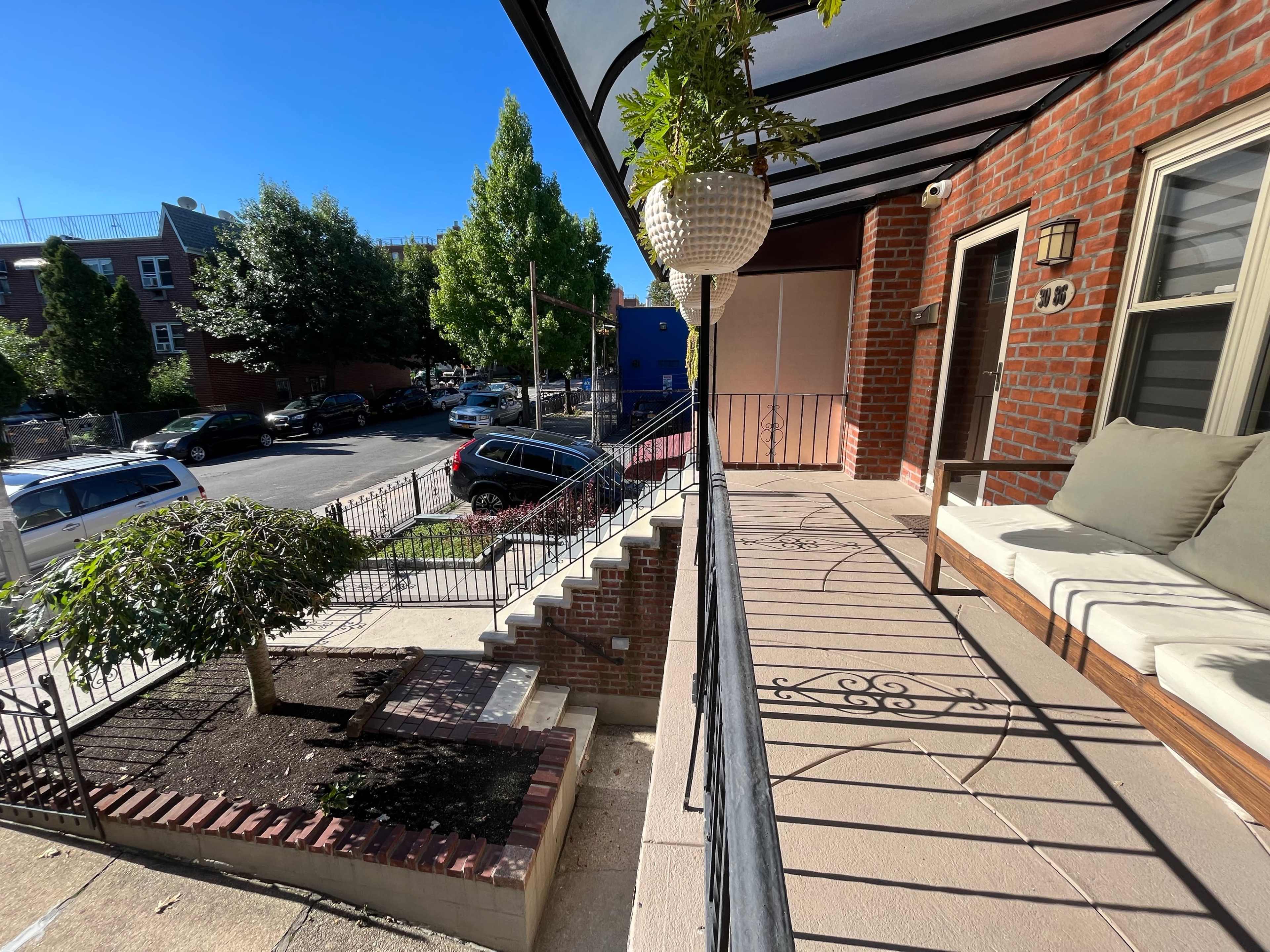 The image shows a patio area with a potted plant, seating, and stairs leading down to a sidewalk next to a street with parked cars.