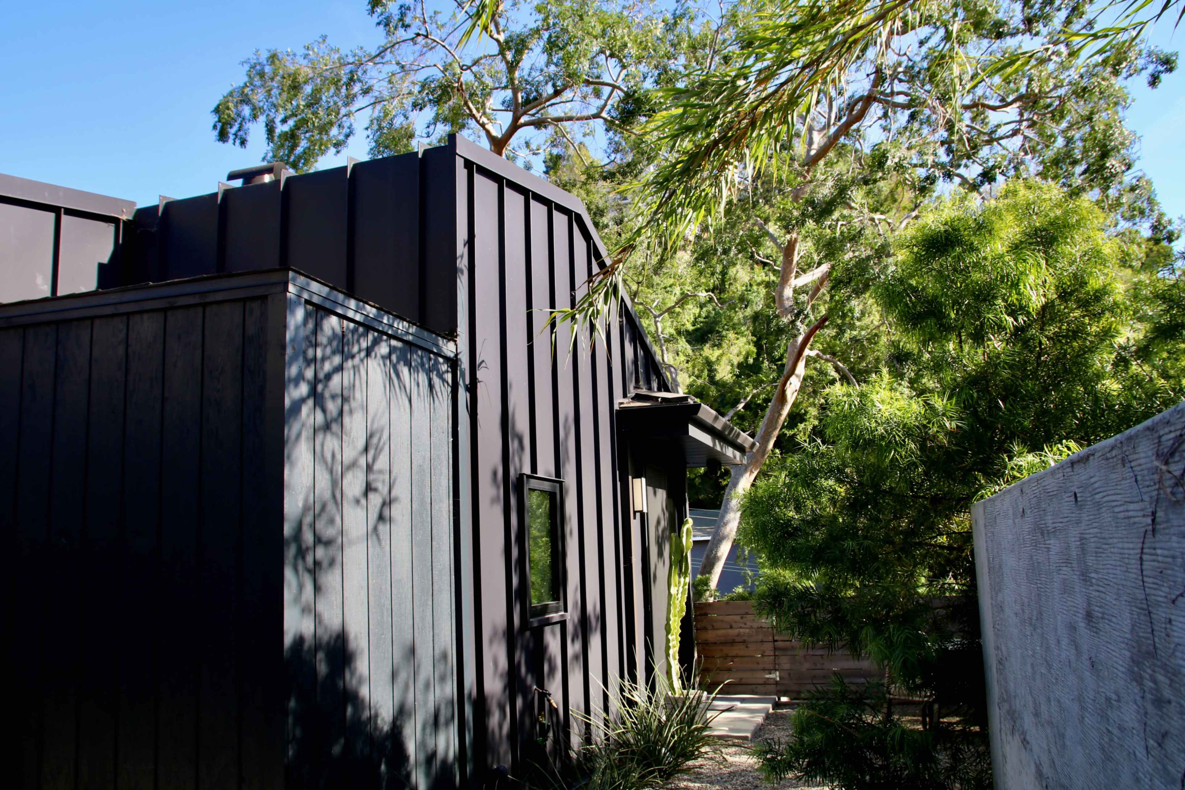 The image shows a modern, black exterior building surrounded by greenery and trees.