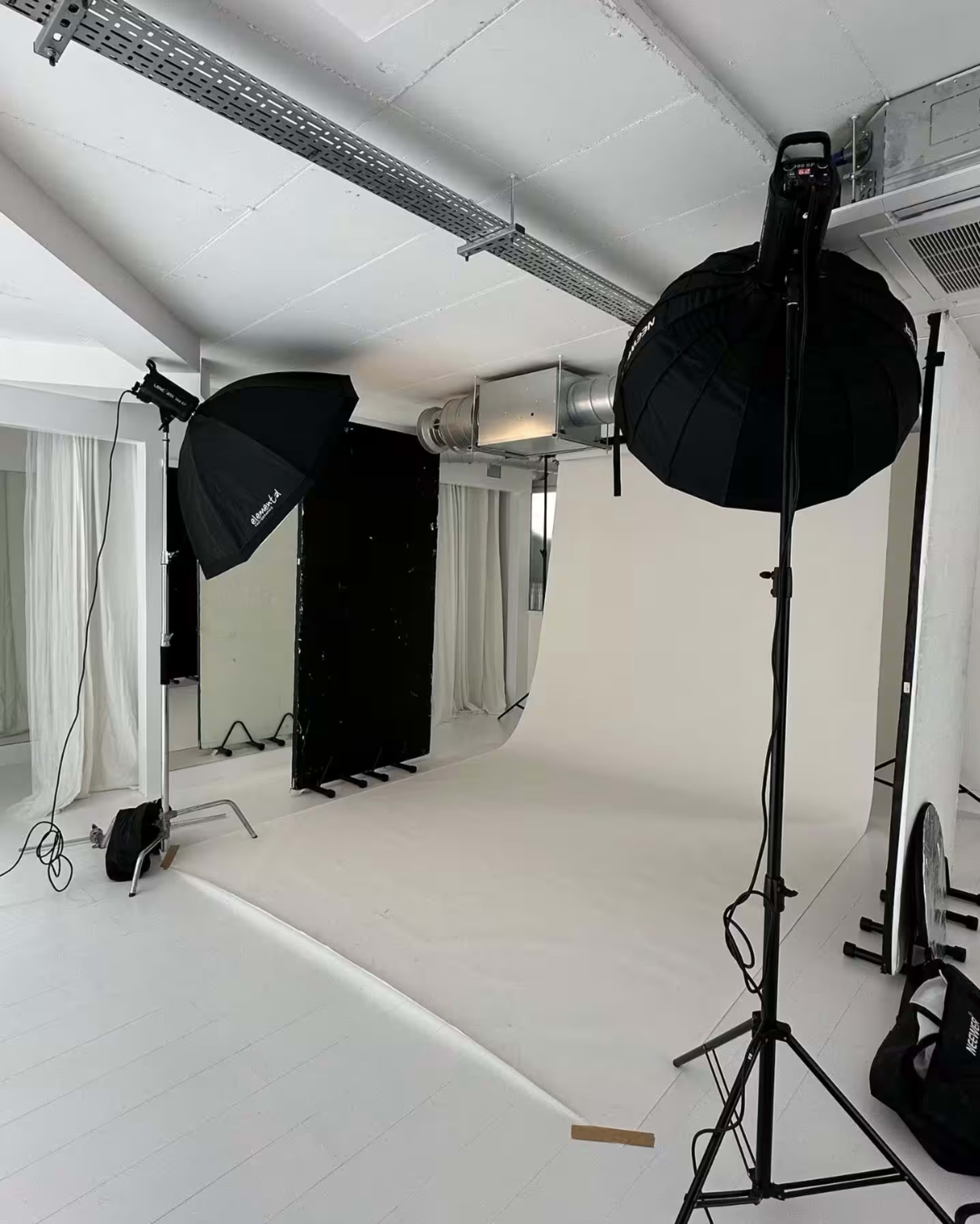 A photography studio setup with two lighting equipment stands and a seamless white backdrop.
