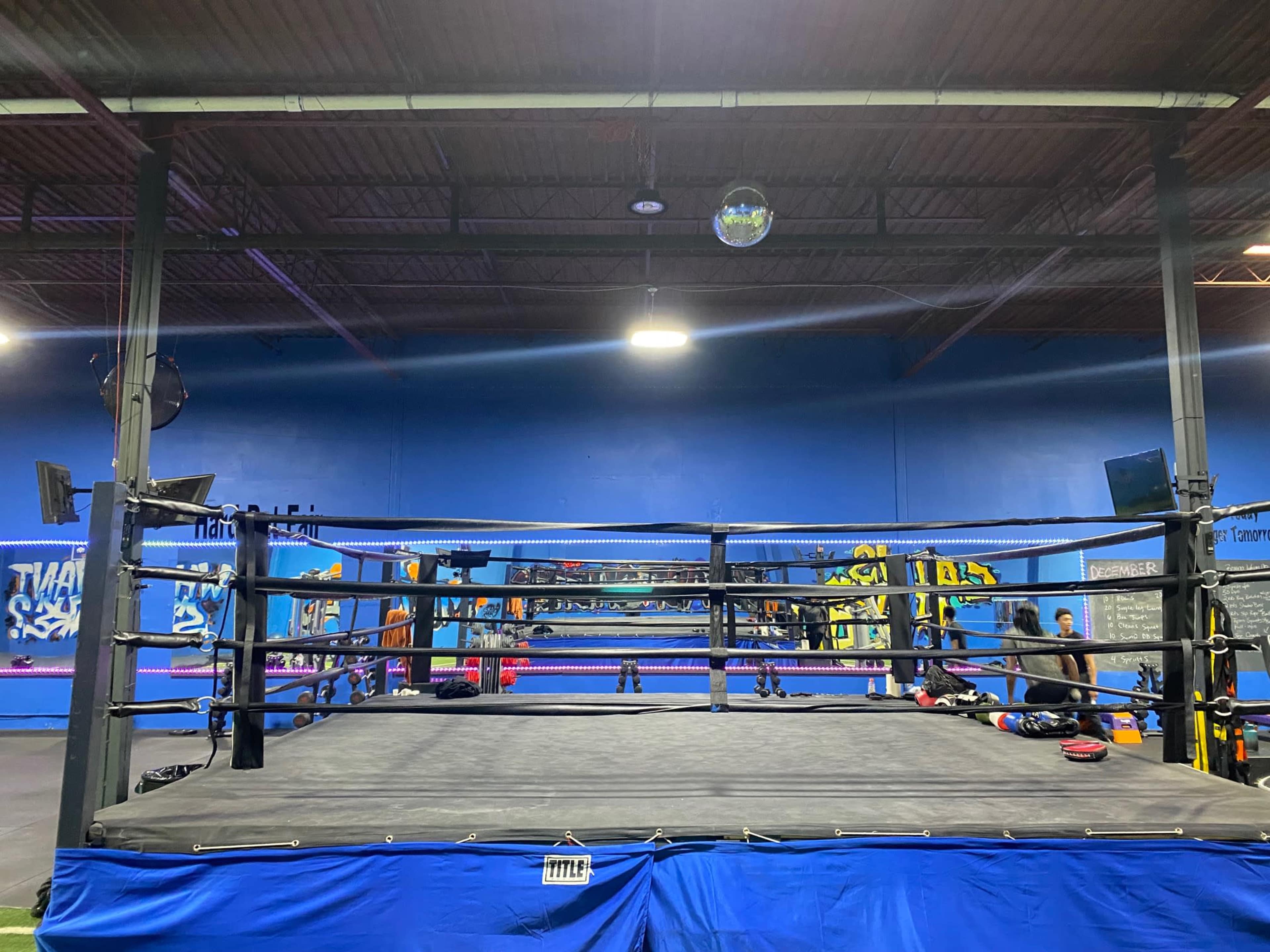 A boxing ring surrounded by various gym equipment in a training facility.