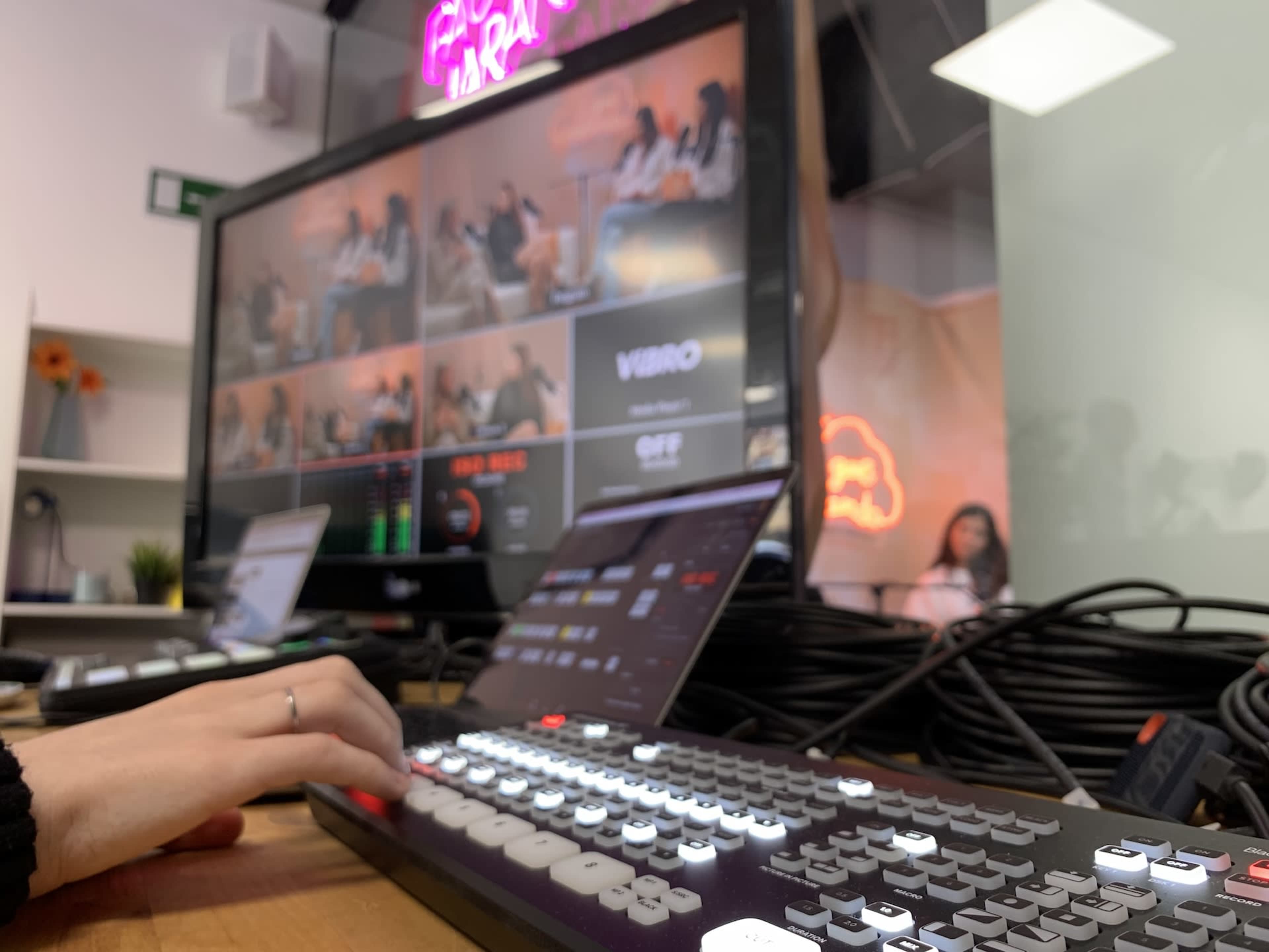 A person is operating a video switcher in front of a large screen displaying multiple camera feeds in a production studio.