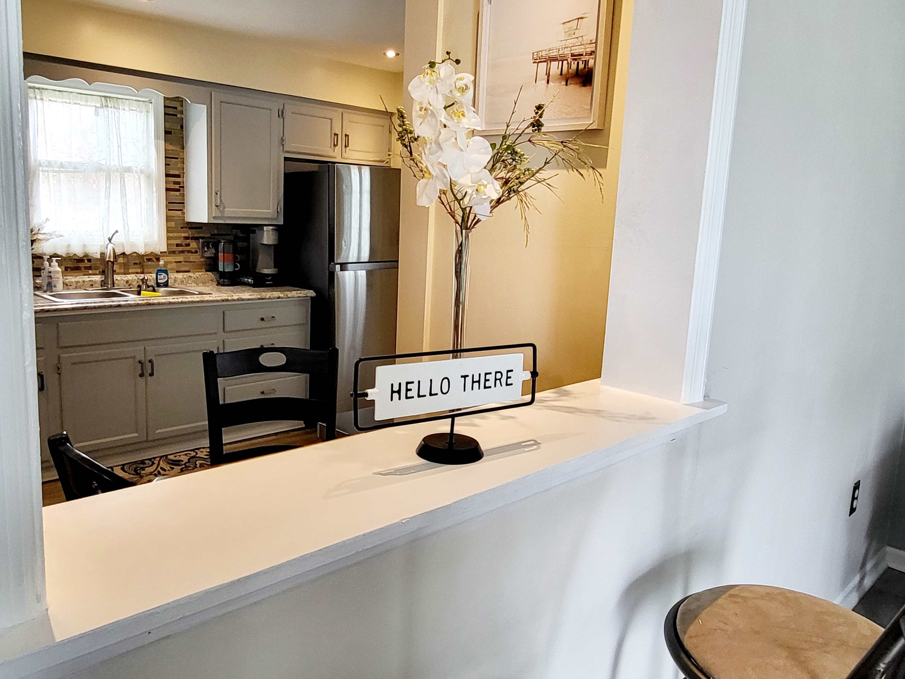 A kitchen with gray cabinets and a decorative sign that reads "HELLO THERE" on a countertop divider.
