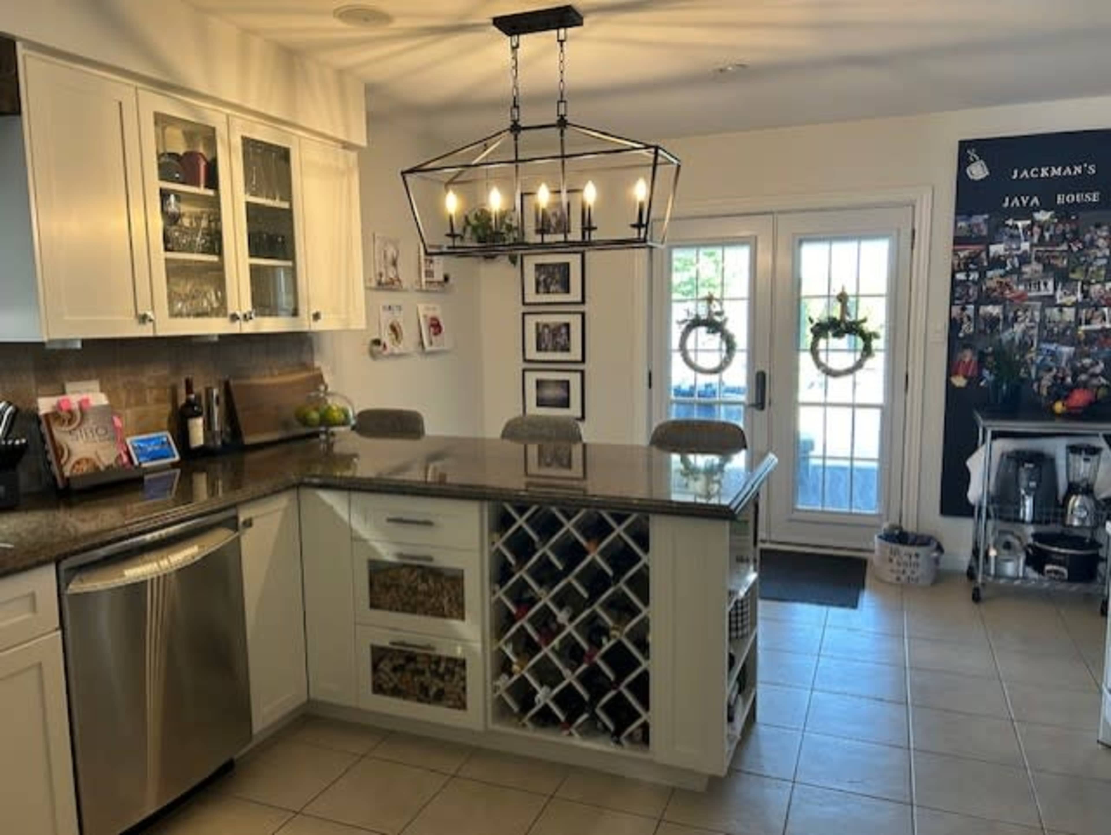 A modern kitchen features white cabinetry, a central island with wine storage, and a large windowed door leading outside.