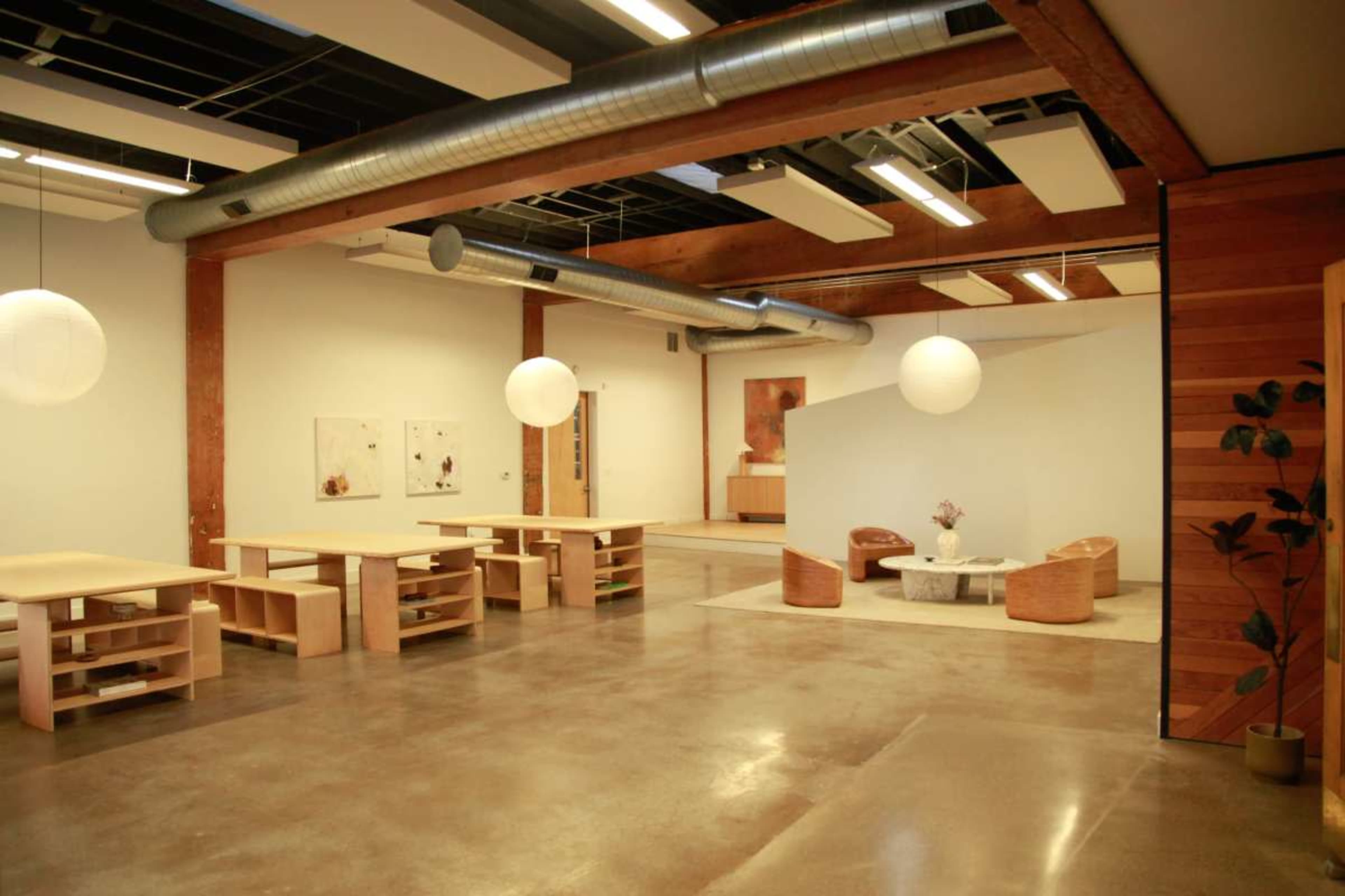 The image shows a spacious interior featuring wooden furniture, polished concrete floors, and large pendant lights, with separate seating areas and artwork on the walls.