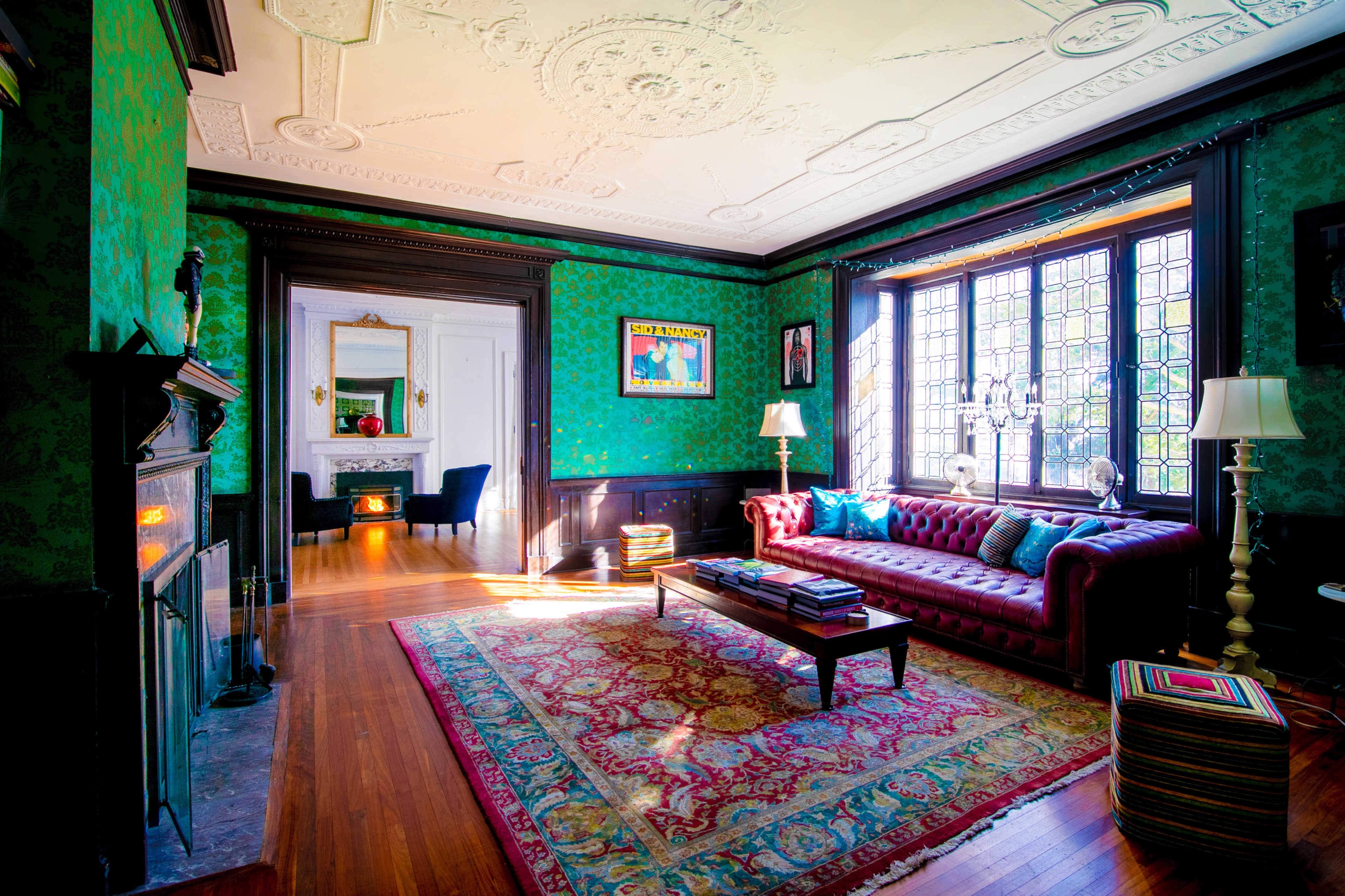 A vibrant green room features a red leather sofa, ornate ceiling, and large windows that allow sunlight to illuminate the space.