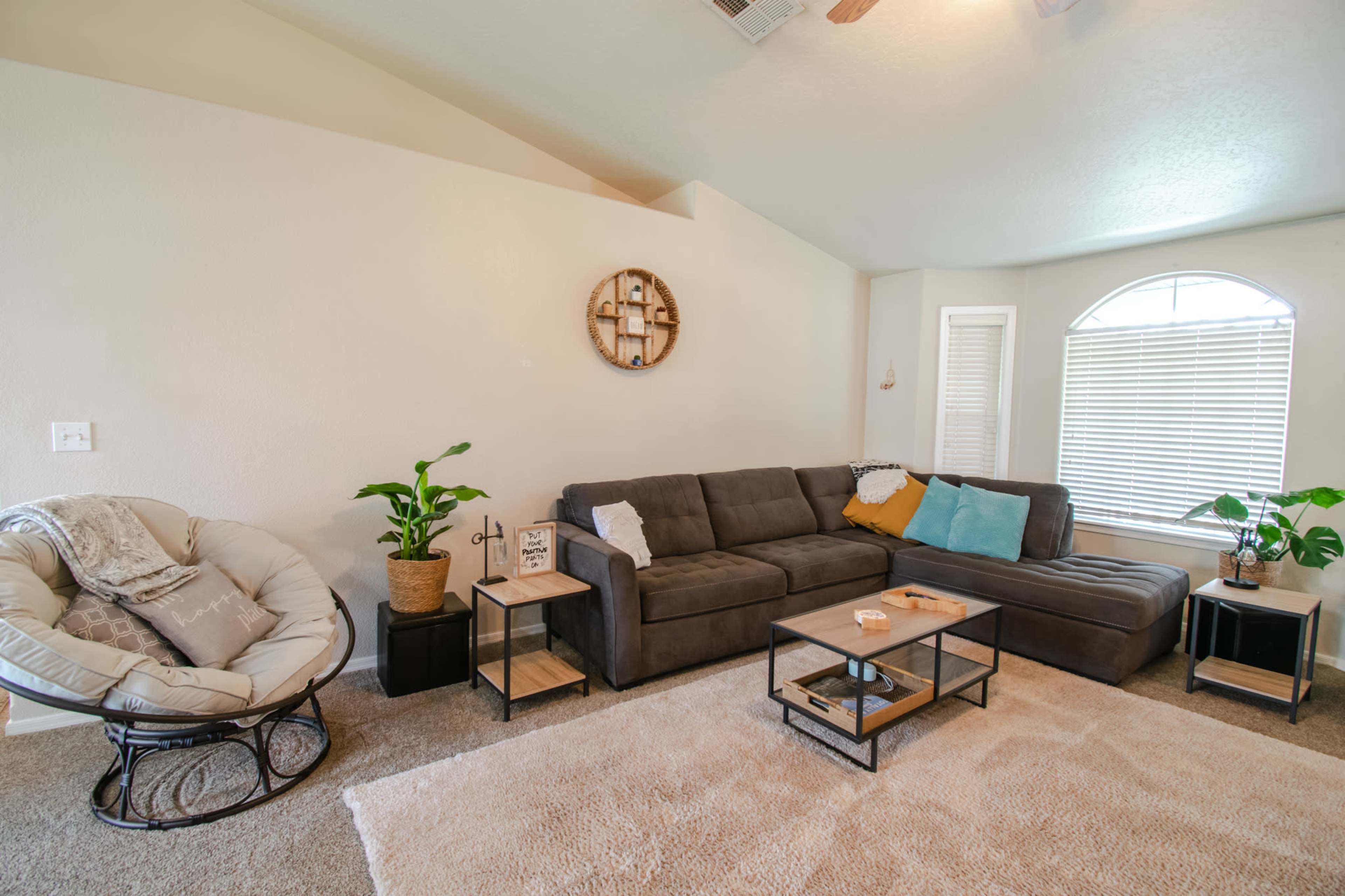 The living room features a sectional sofa, a round chair, a coffee table, and large windows with natural light.