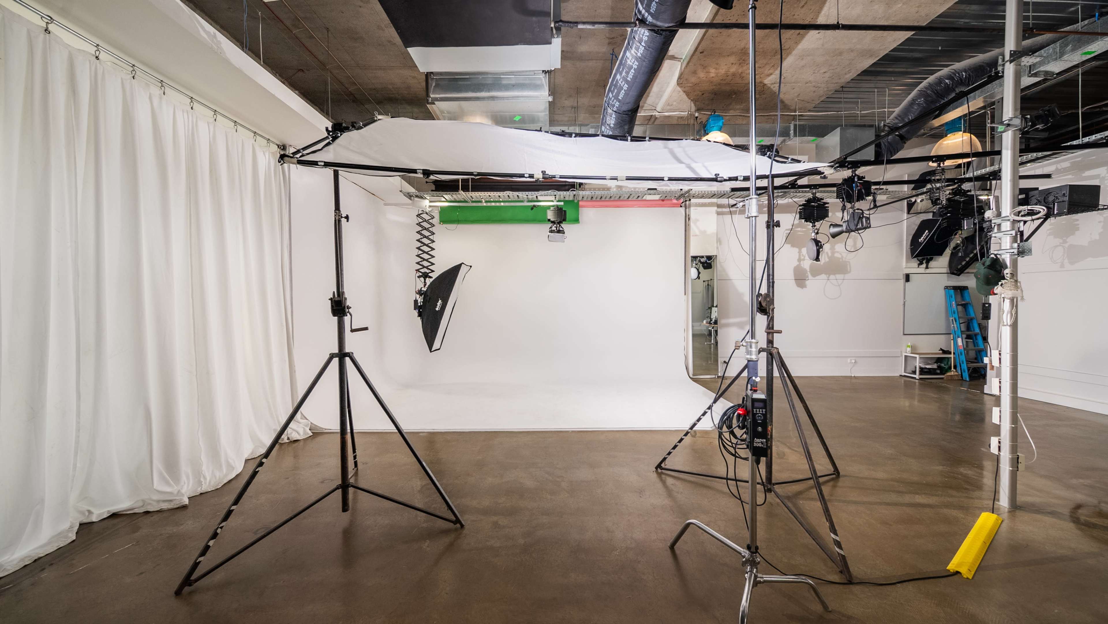 The image shows a photography studio setup with a white backdrop, lighting equipment, and support stands.