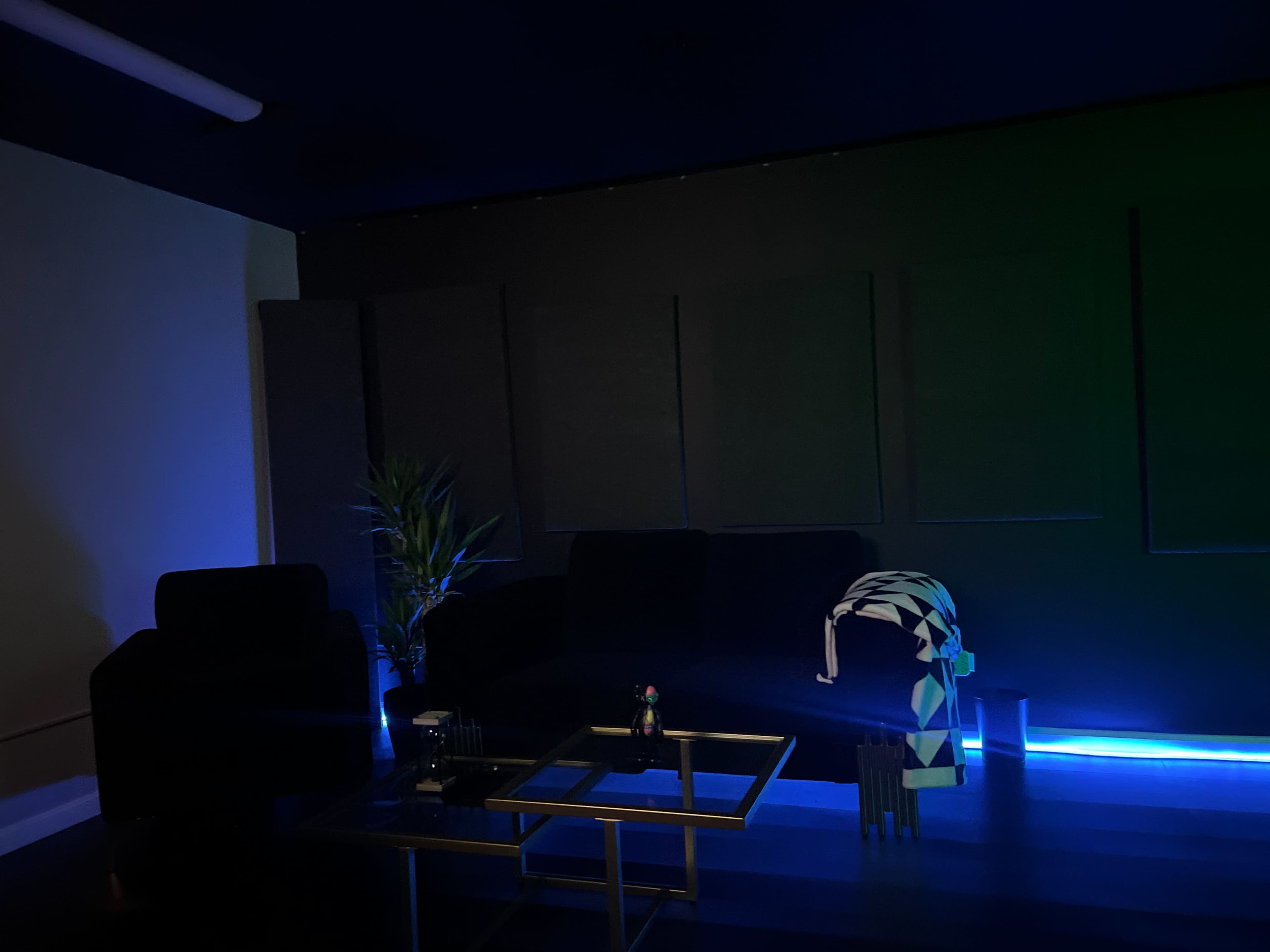 A dimly lit room with a black sofa, a coffee table, a decorative plant, and blue LED lighting along the bottom of the walls.