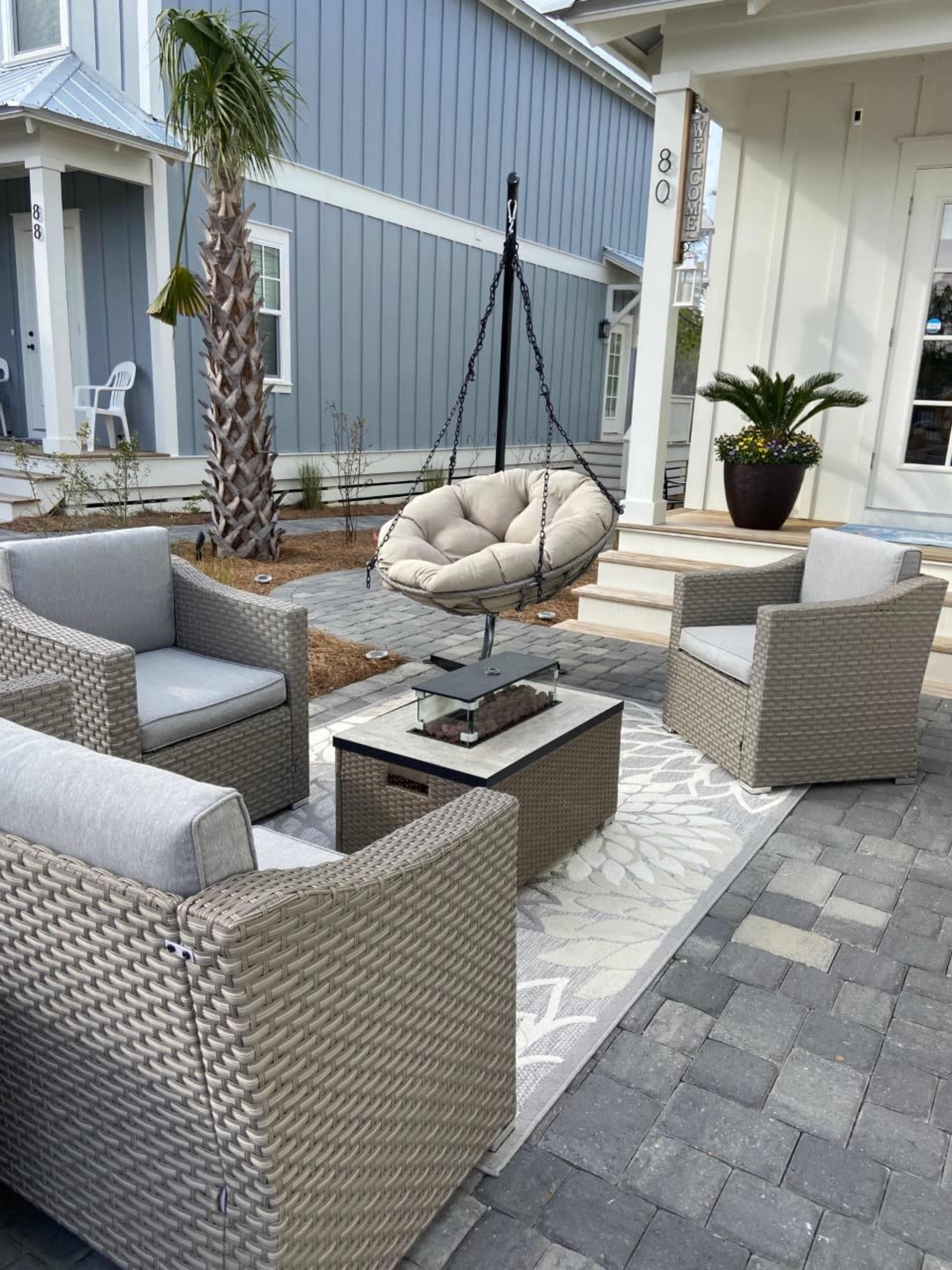 A cozy outdoor seating area with four wicker chairs surrounding a small table and a hanging chair suspended nearby.