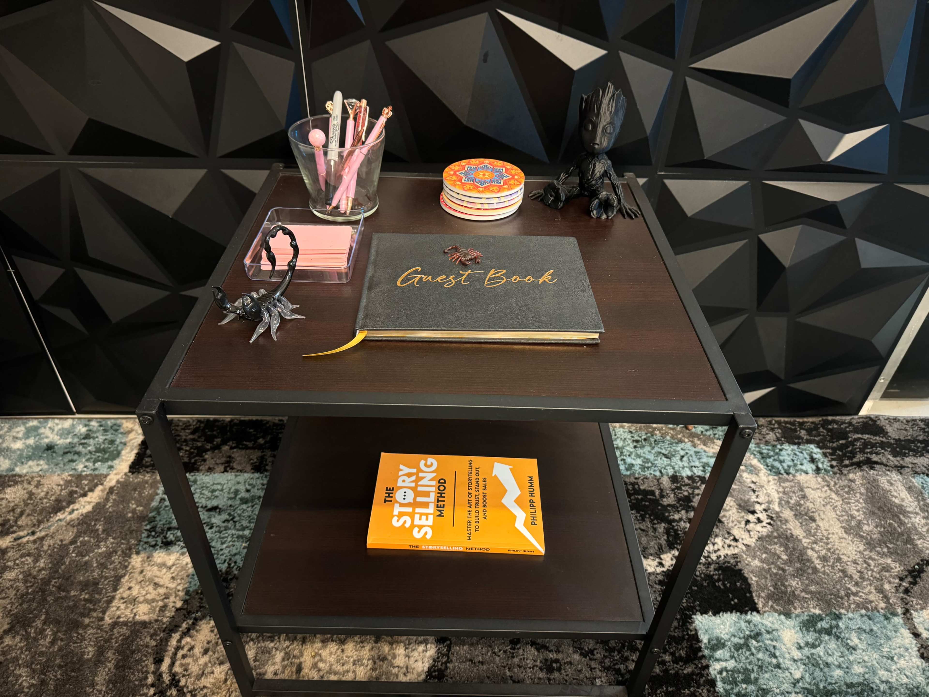 A wooden side table features a guest book, a decorative coaster, a pack of sticky notes, and a book titled "The Story of Selling."