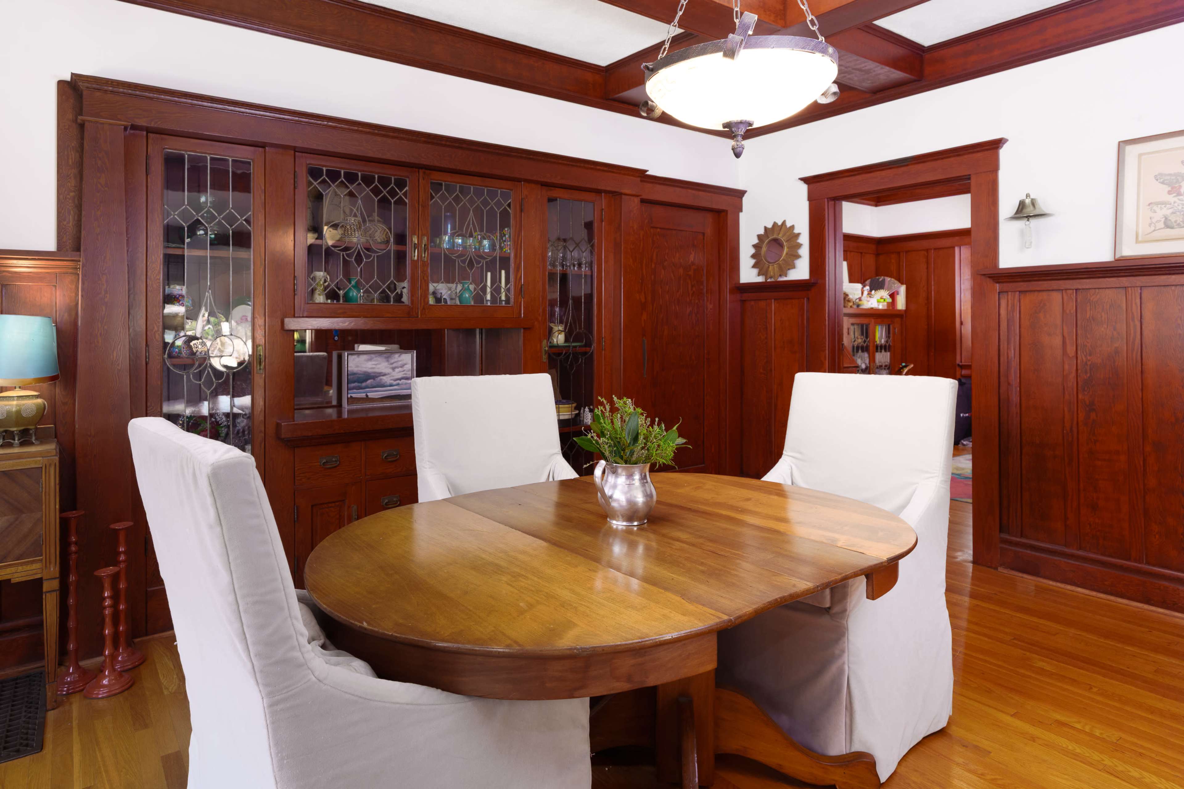A wooden dining table with three chairs is positioned in a room featuring dark wood paneling and built-in cabinetry.