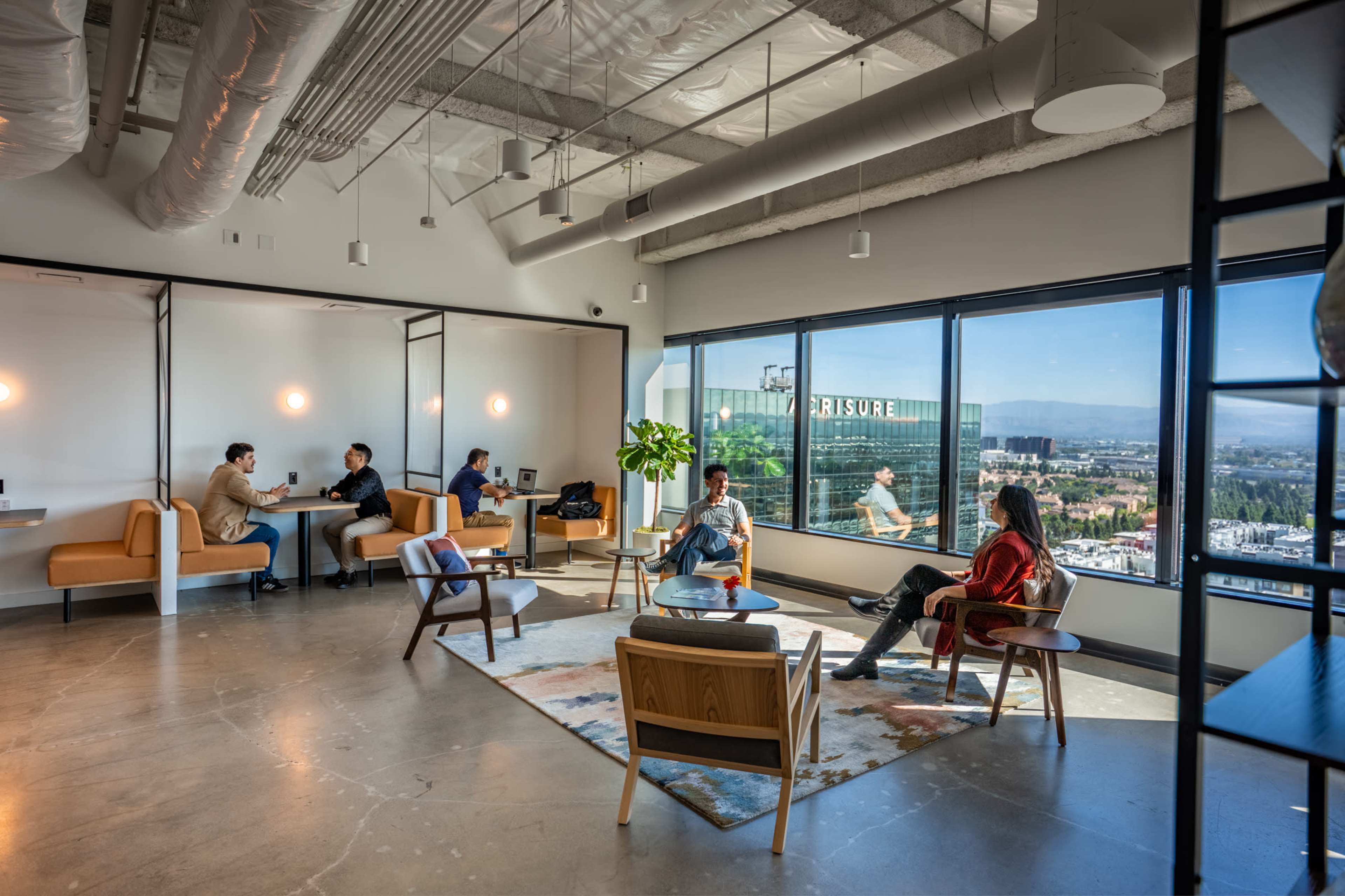A modern office space features several groups of people engaged in conversation, with large windows overlooking a cityscape.