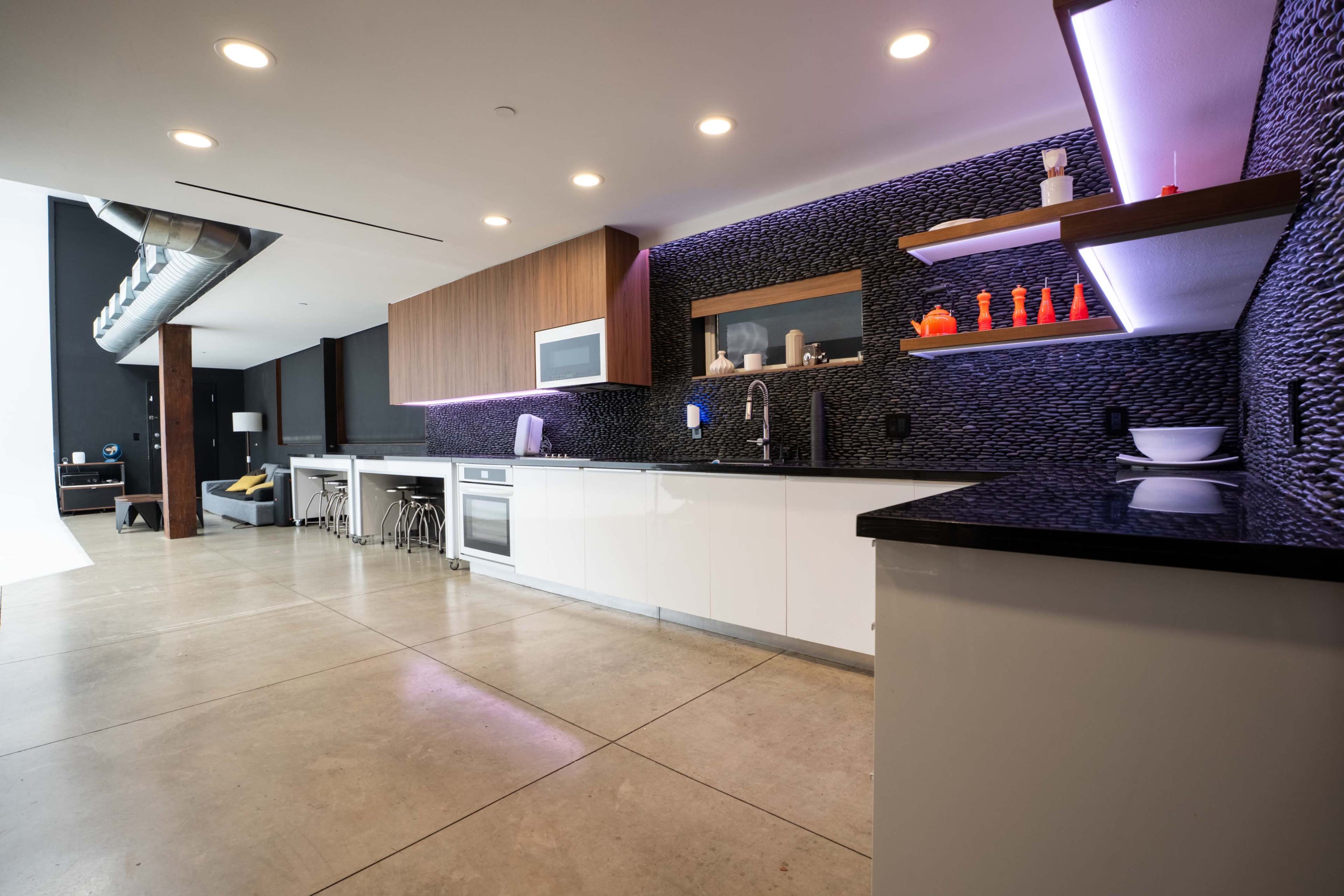 The image shows a modern kitchen with sleek white cabinets, a black countertop, and backlit shelves displaying decorative items.