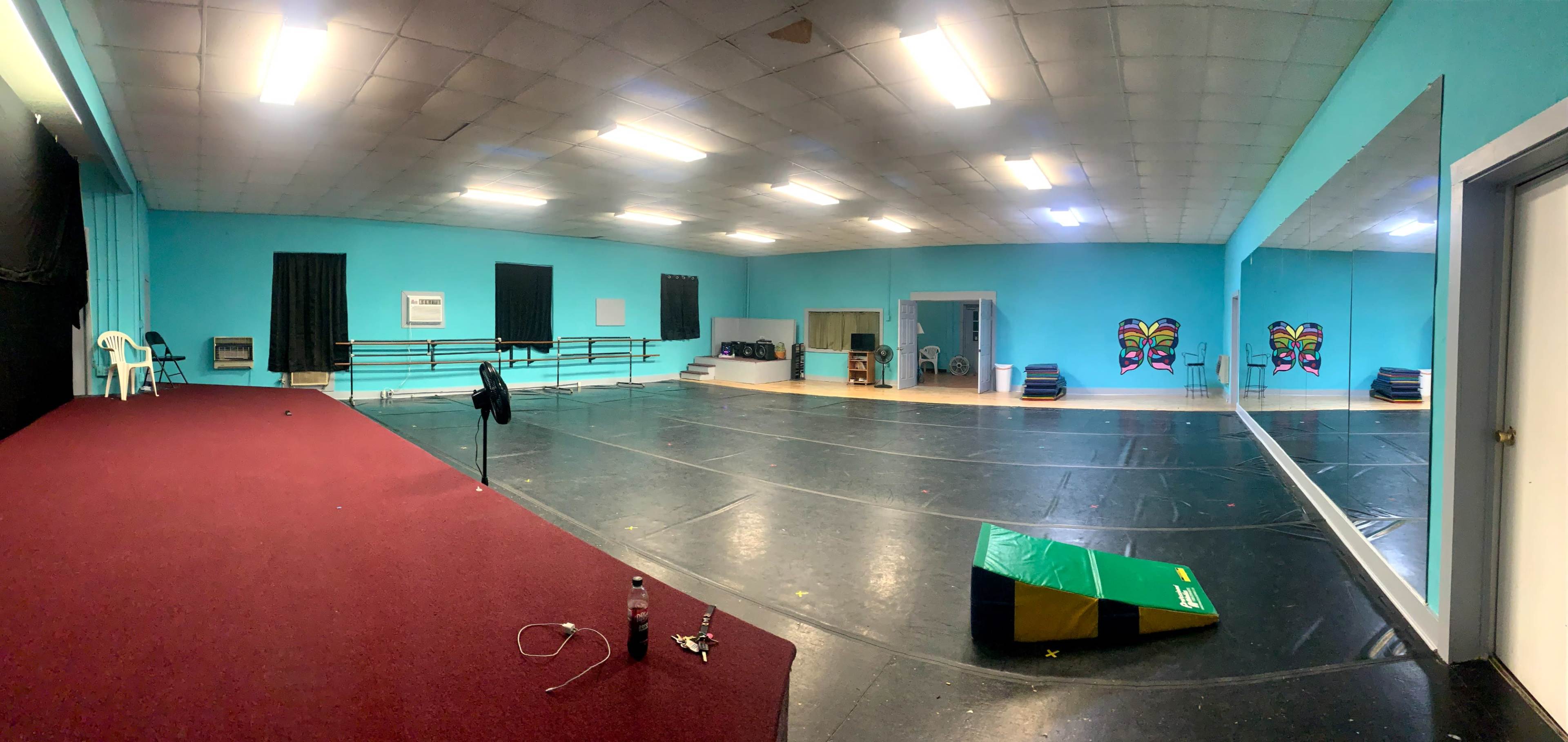A spacious dance studio with turquoise walls, a black floor, and mirrored walls, featuring a red carpet area and various colorful decorations.