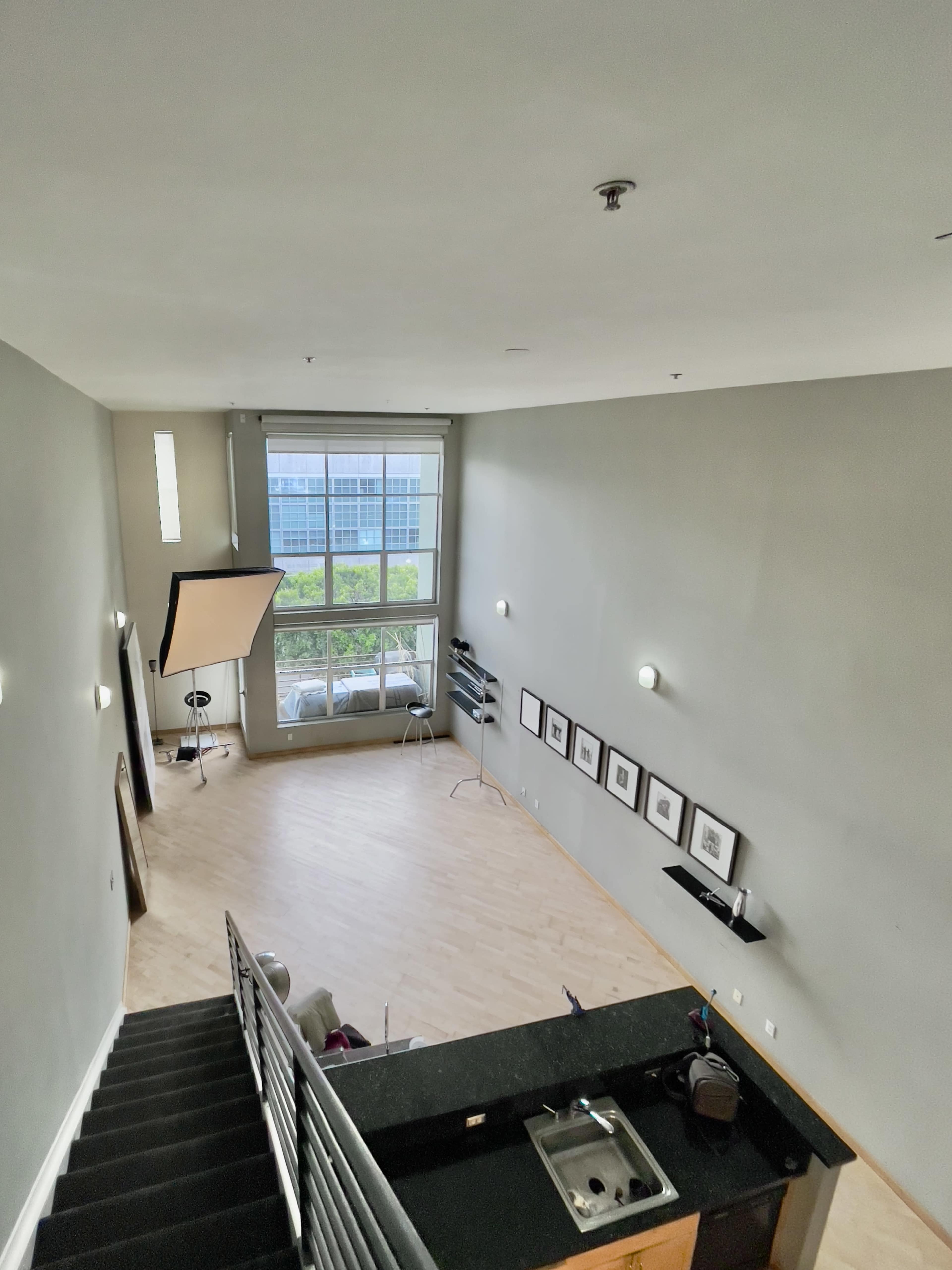 An open space interior with a staircase leading down to a lower level that features a kitchen area and large windows allowing natural light.