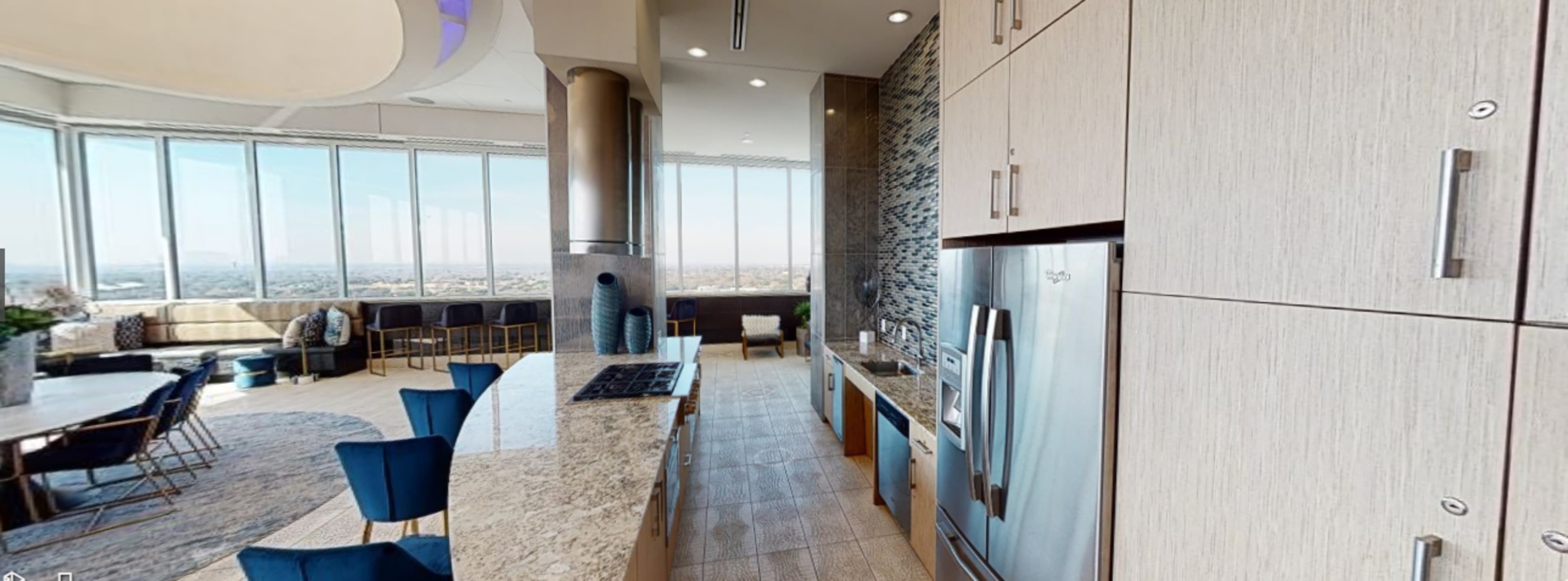 A modern kitchen with granite countertops, stainless steel appliances, and a view of the city through large windows.
