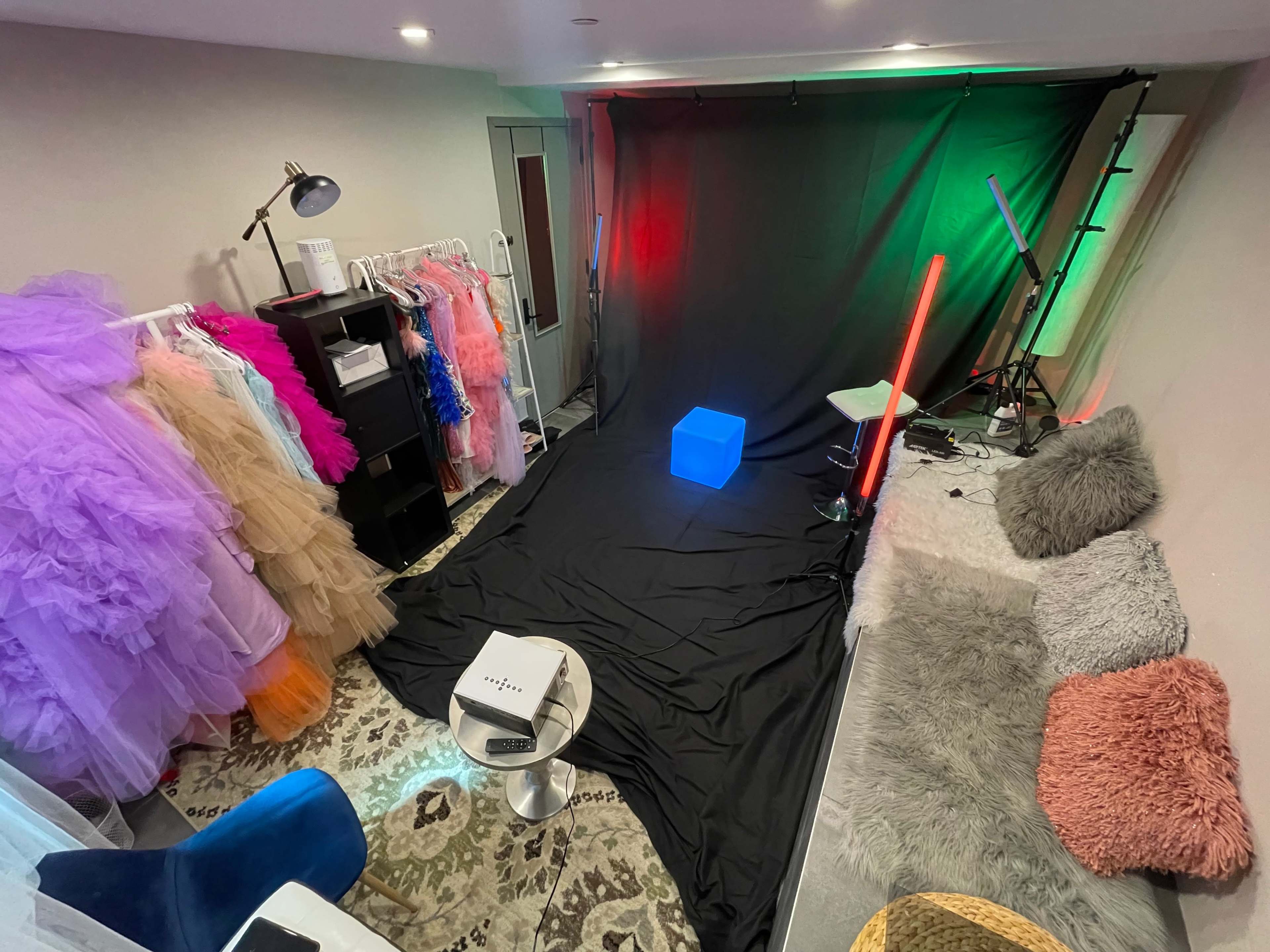 A photography studio setup with colorful dresses on hangers, a black backdrop, and various lighting equipment.
