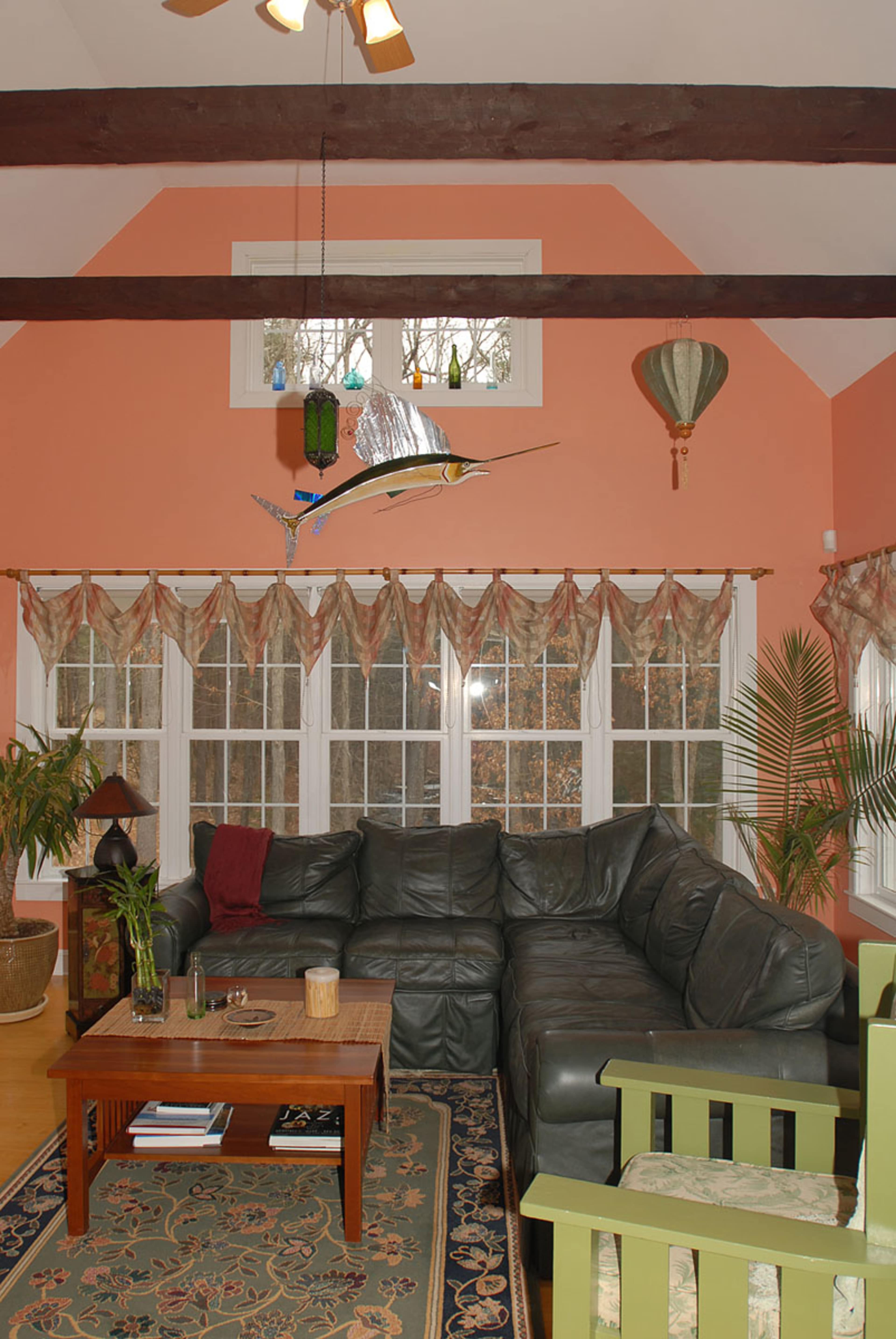 The living room features a large dark green sectional sofa, a wooden coffee table, and multiple windows adorned with patterned curtains.