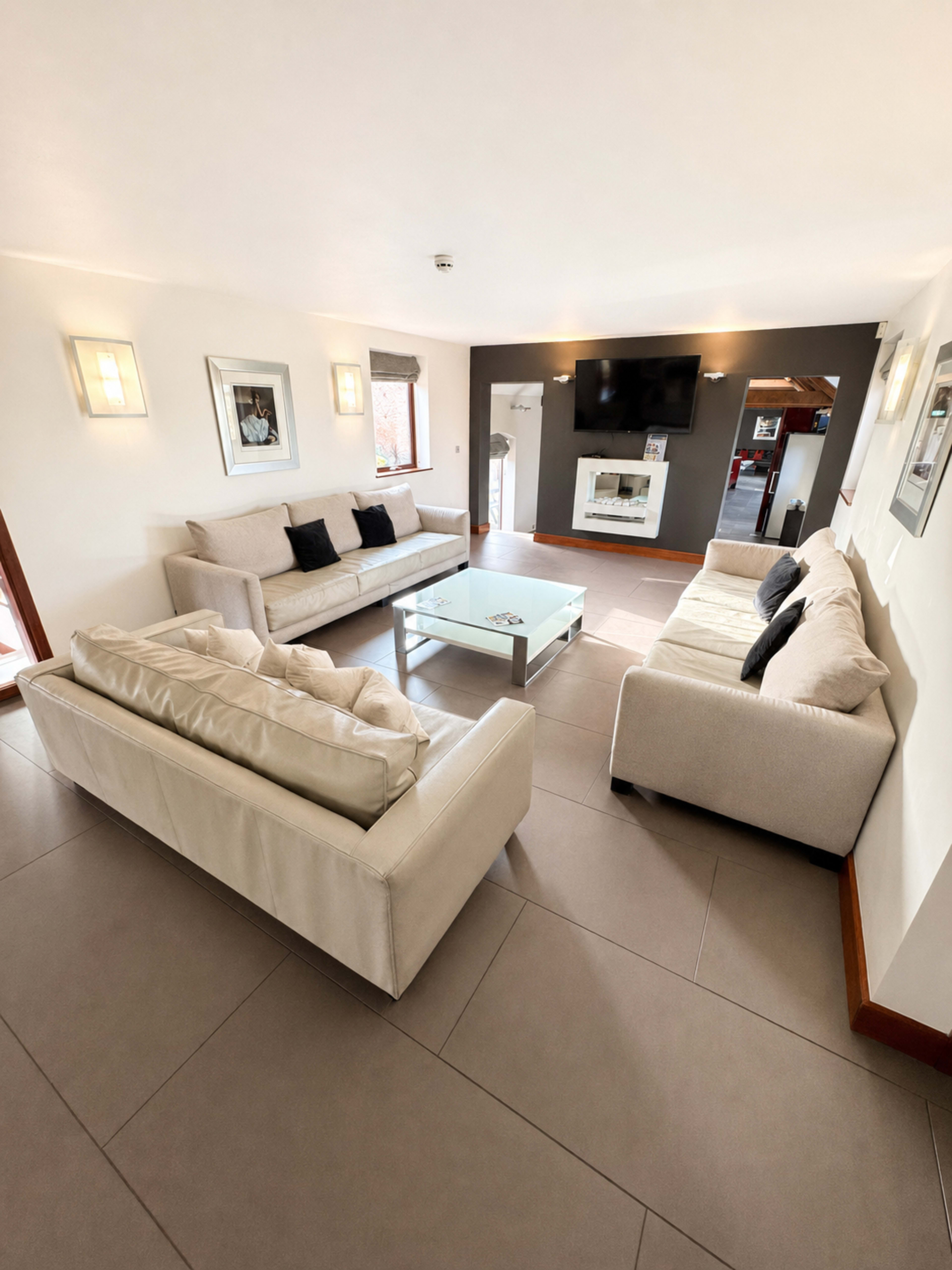 The image shows a modern living room with two sofas, a glass coffee table, and a television mounted on the wall.