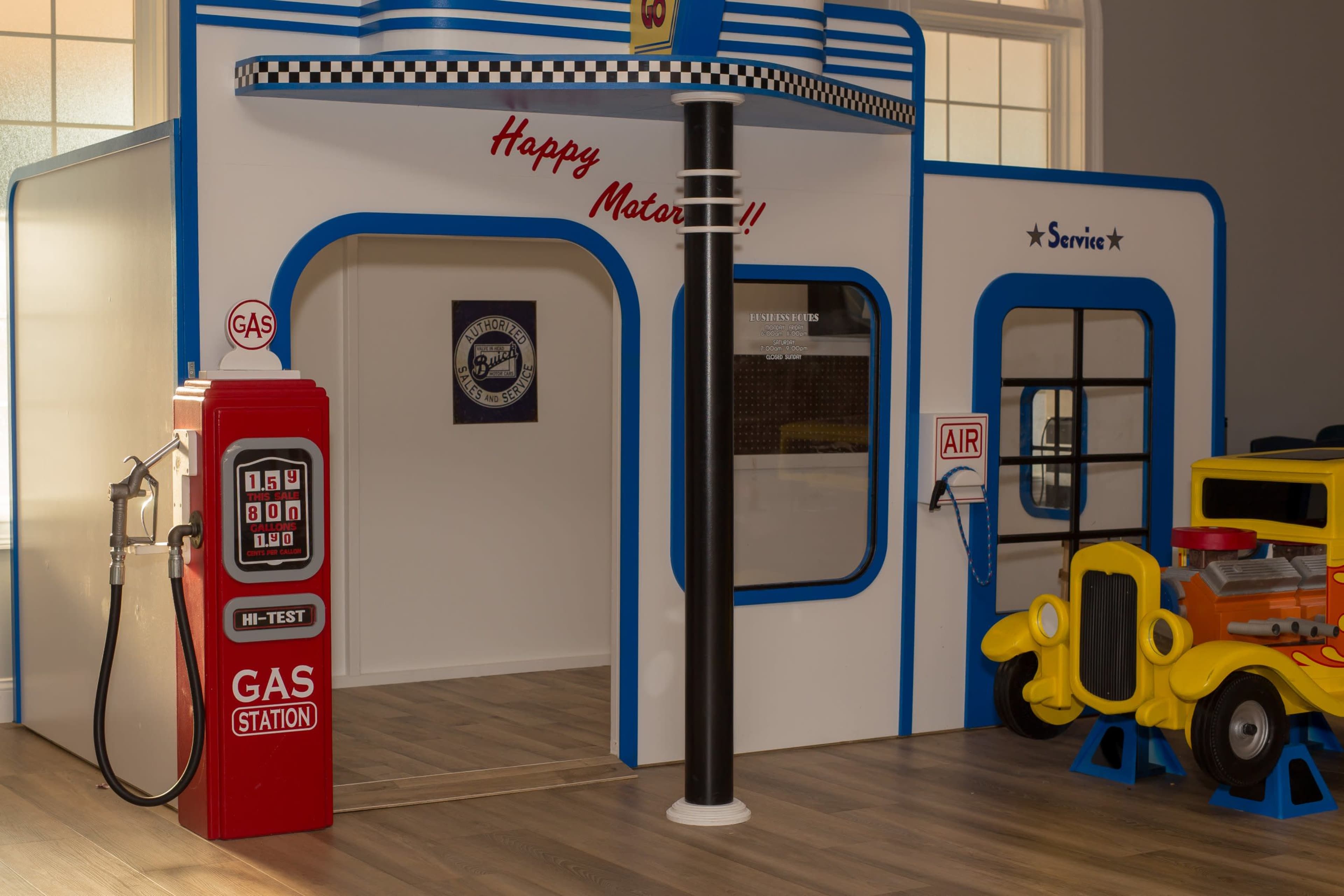 The image shows a colorful toy gas station with a retro gas pump, a service area, and a toy car parked nearby.
